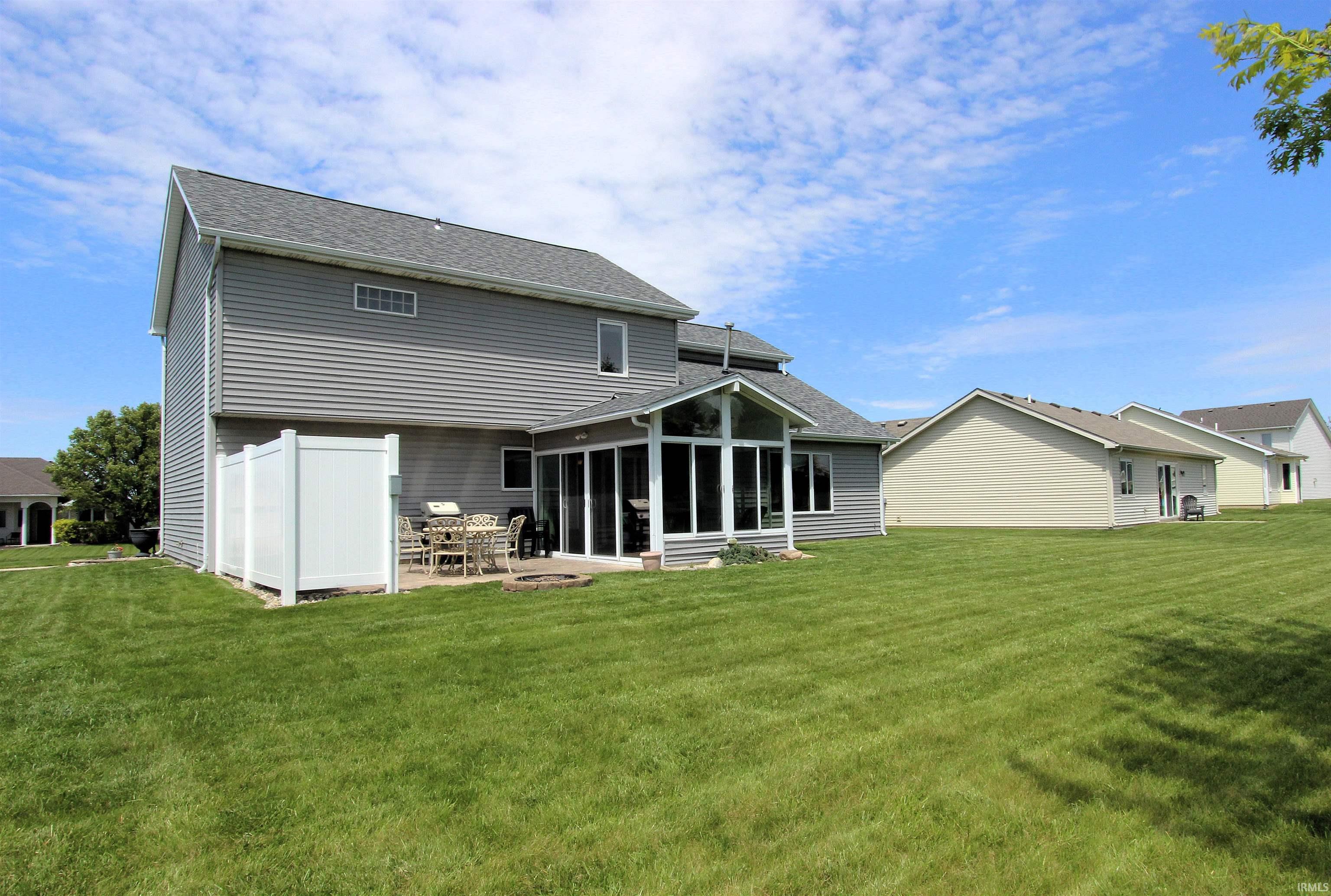 Expansive green lawn surrounds the property, featuring a gray siding exterior and a sunroom with large windows