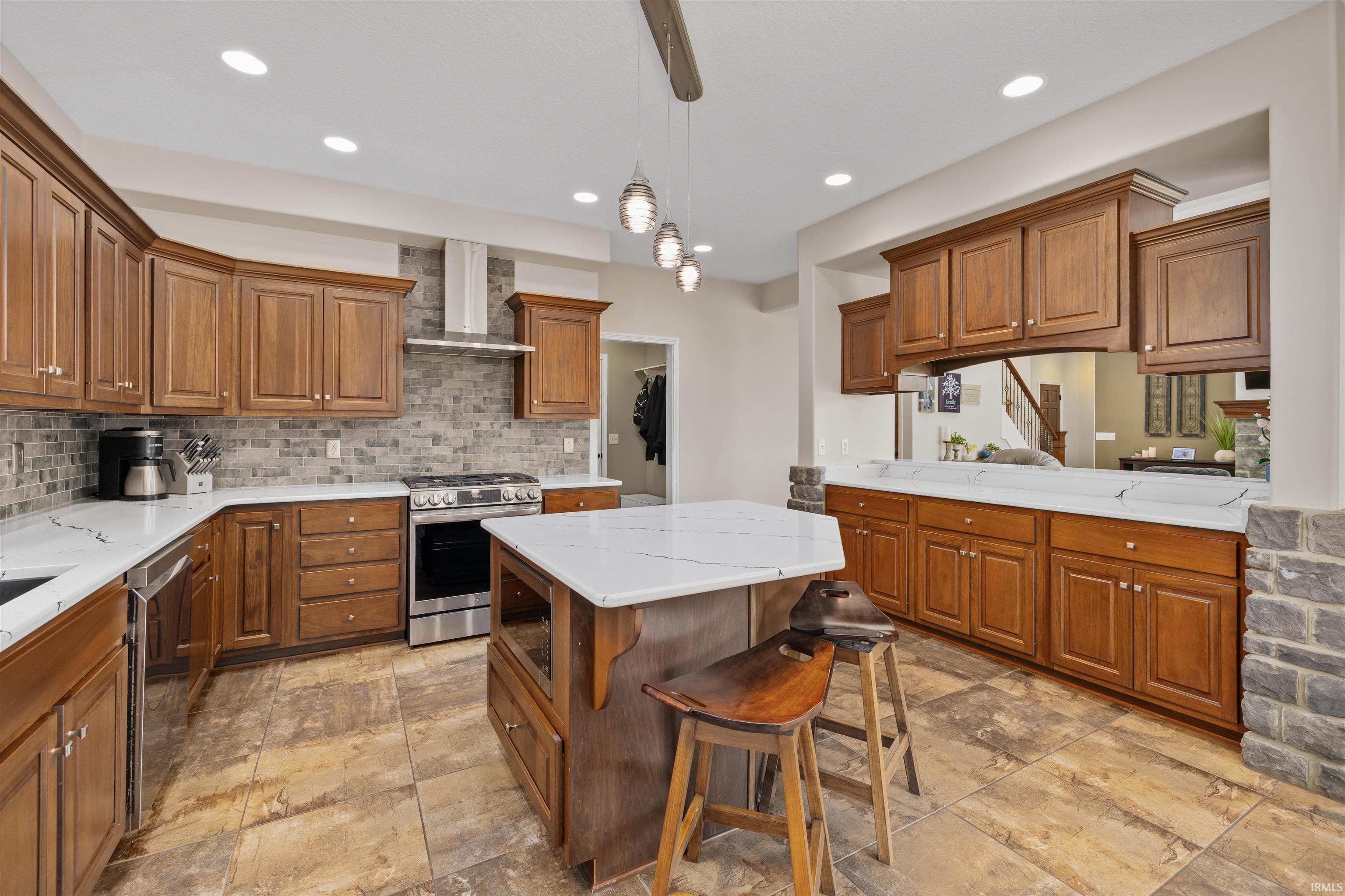 Open kitchen featuring a central island with countertop seating, wood-finish cabinetry, stainless steel appliances, white countertops, and a stone tile backsplash