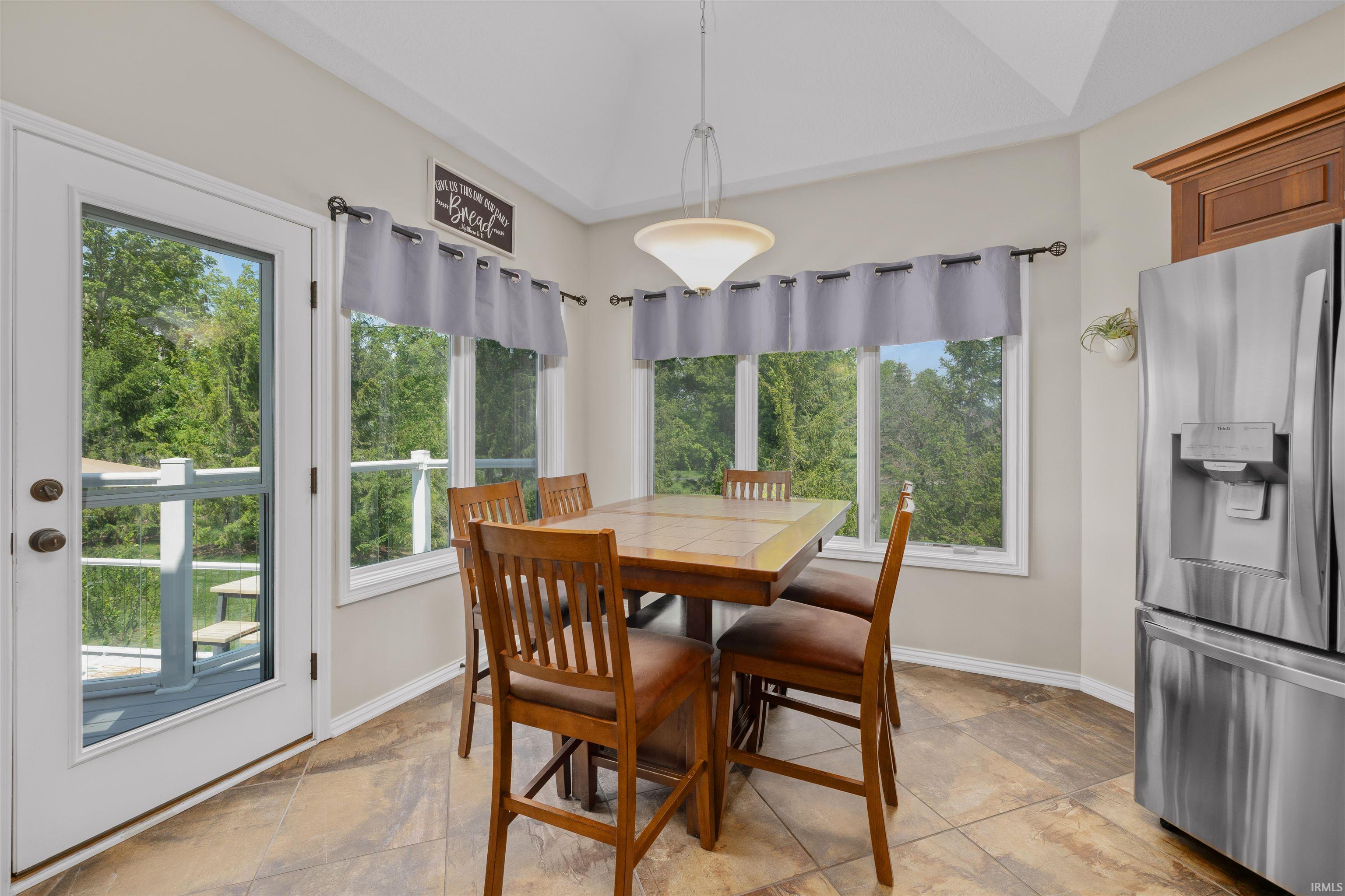 Dining area with vaulted ceiling, tiled flooring, an exterior door providing deck access, multiple windows, and a stainless steel refrigerator