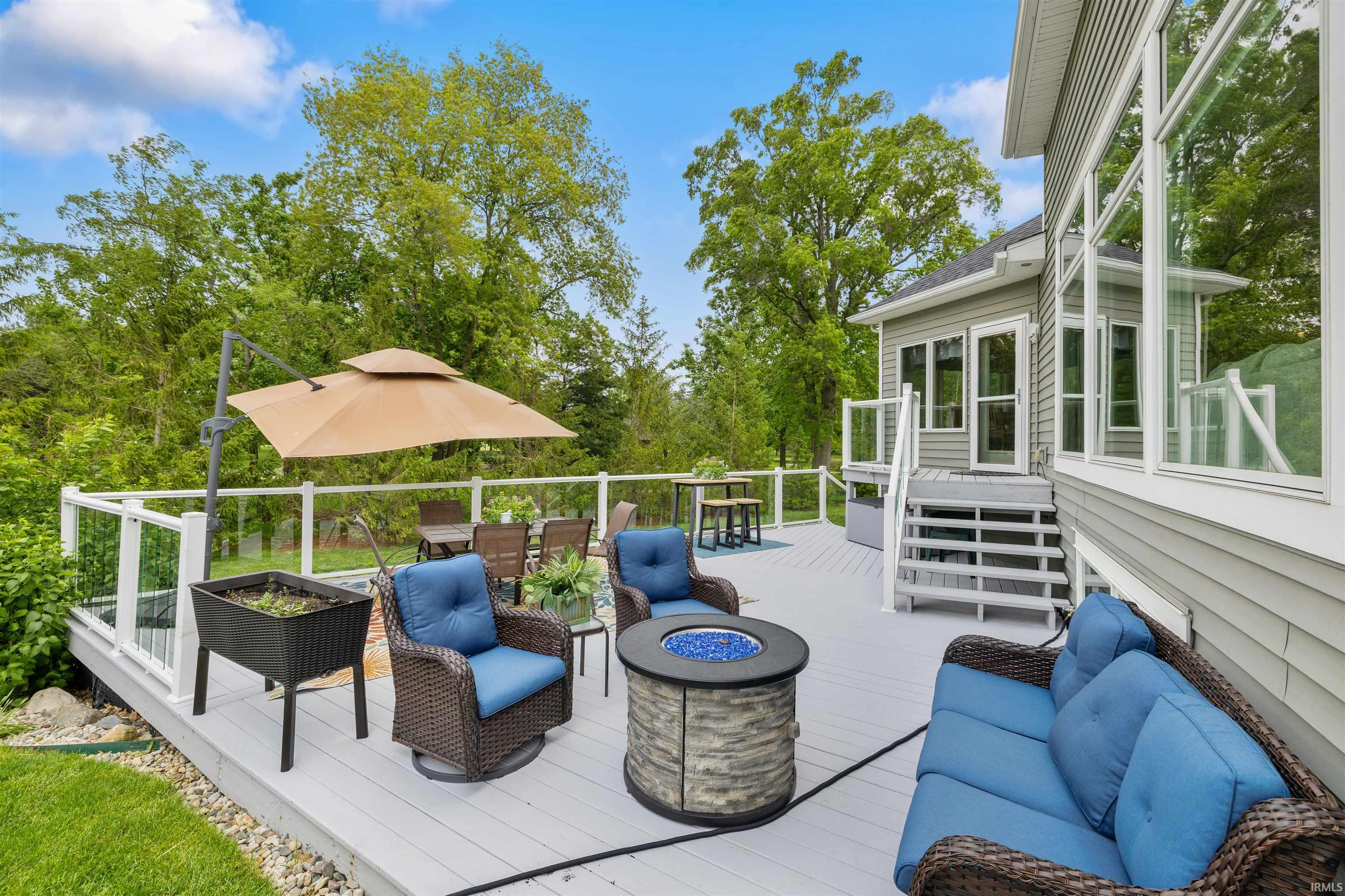 Spacious outdoor deck featuring gray composite decking, glass panel railings, and a built-in fire pit