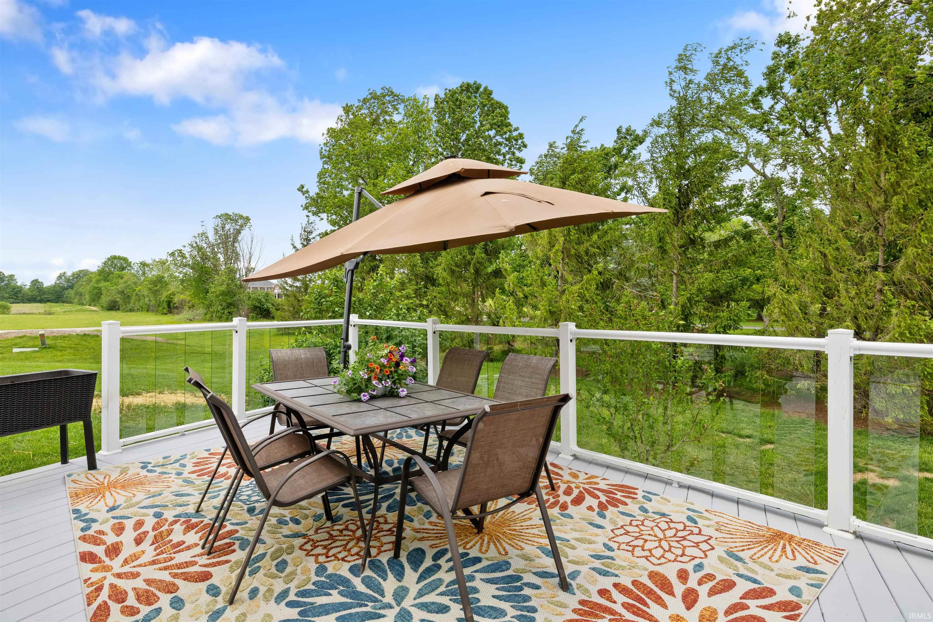 Spacious outdoor deck featuring light gray composite decking and a clear glass panel railing system overlooking mature trees and open green space