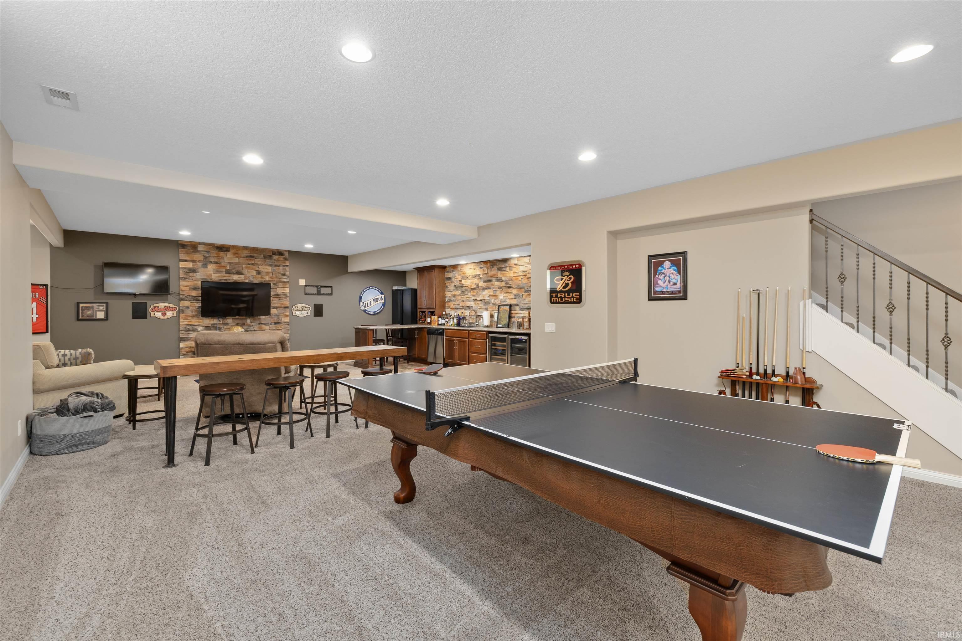 Spacious lower-level entertainment area featuring recessed lighting, a stone accent wall, and a built-in wet bar with wood cabinetry and stainless steel appliances