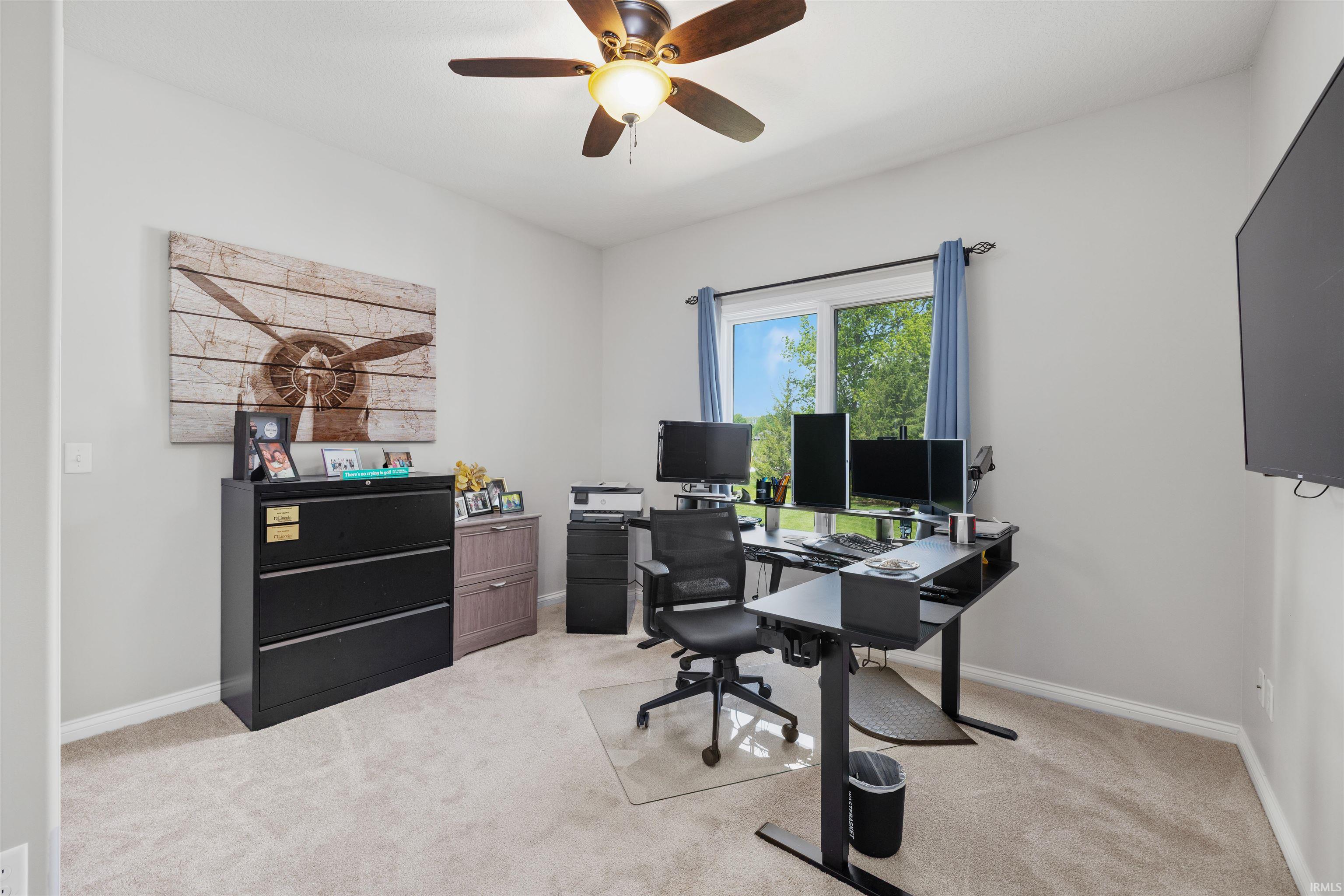 Neutral wall paint with carpet flooring, a ceiling fan with light fixture, and a large window with blue drapes