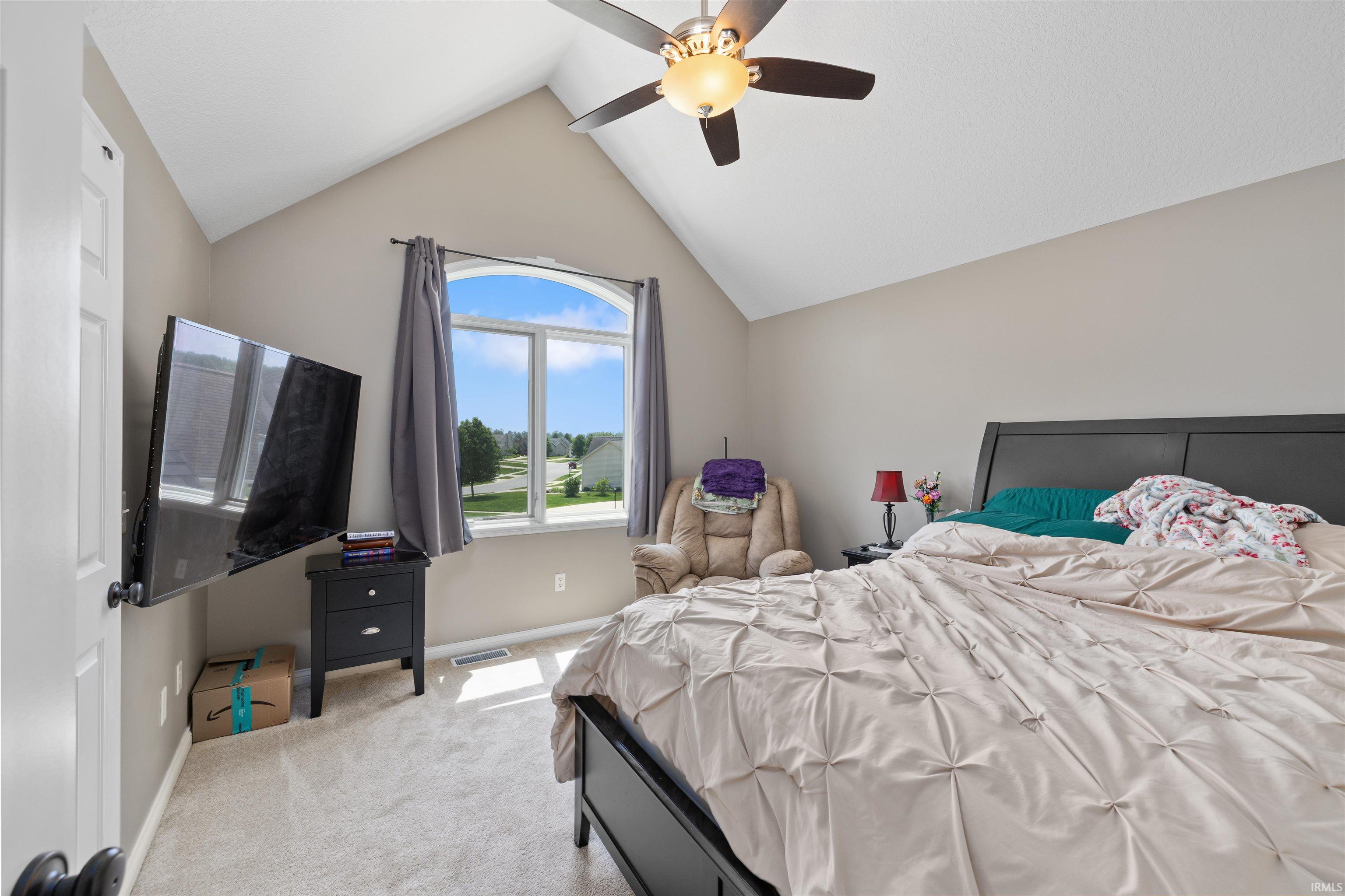 Vaulted ceiling bedroom with arched window, neutral carpeting, and a ceiling fan with integrated lighting