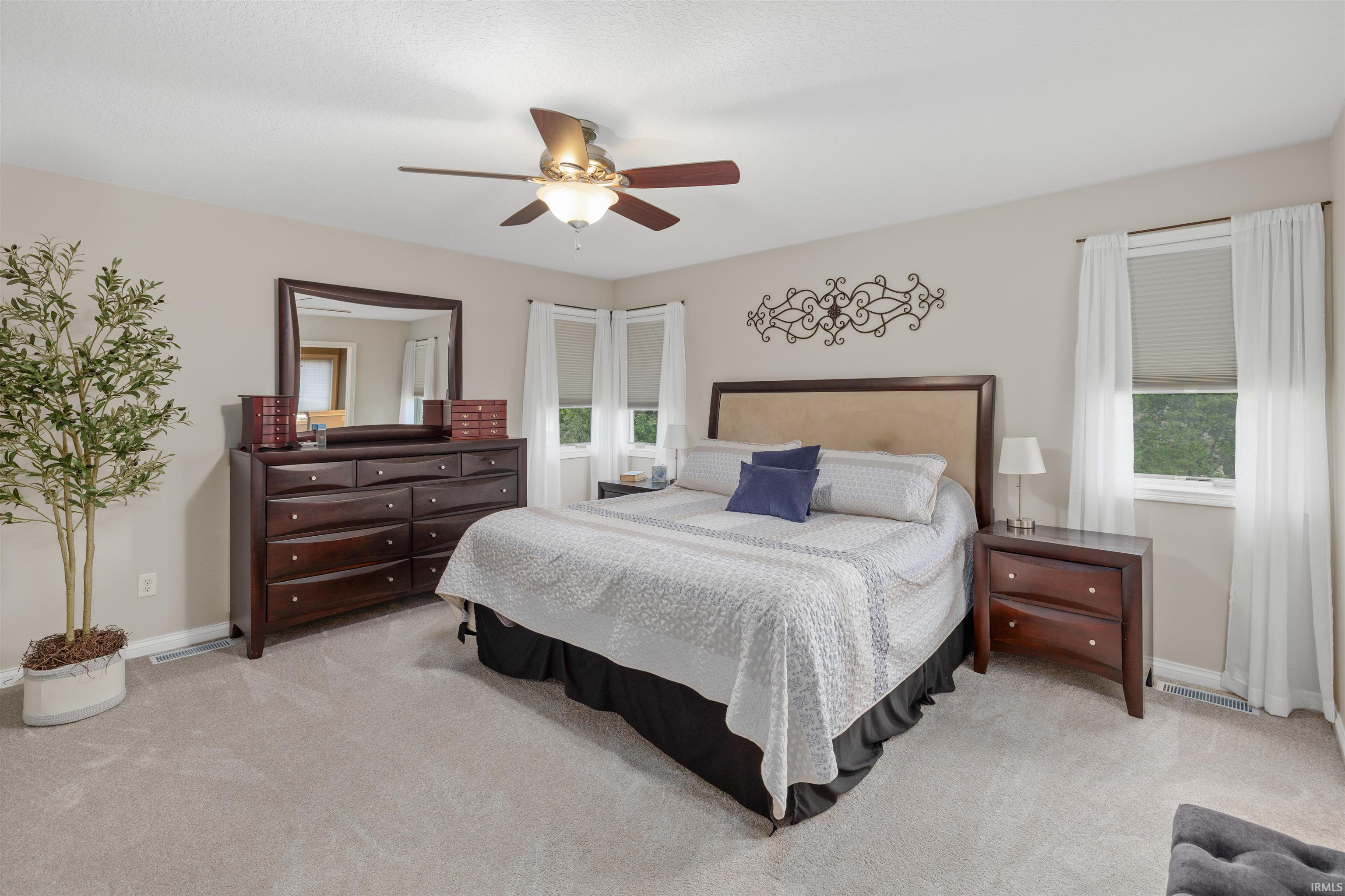 Carpeted bedroom with a bay window, ceiling fan with integrated lighting, and neutral wall tones