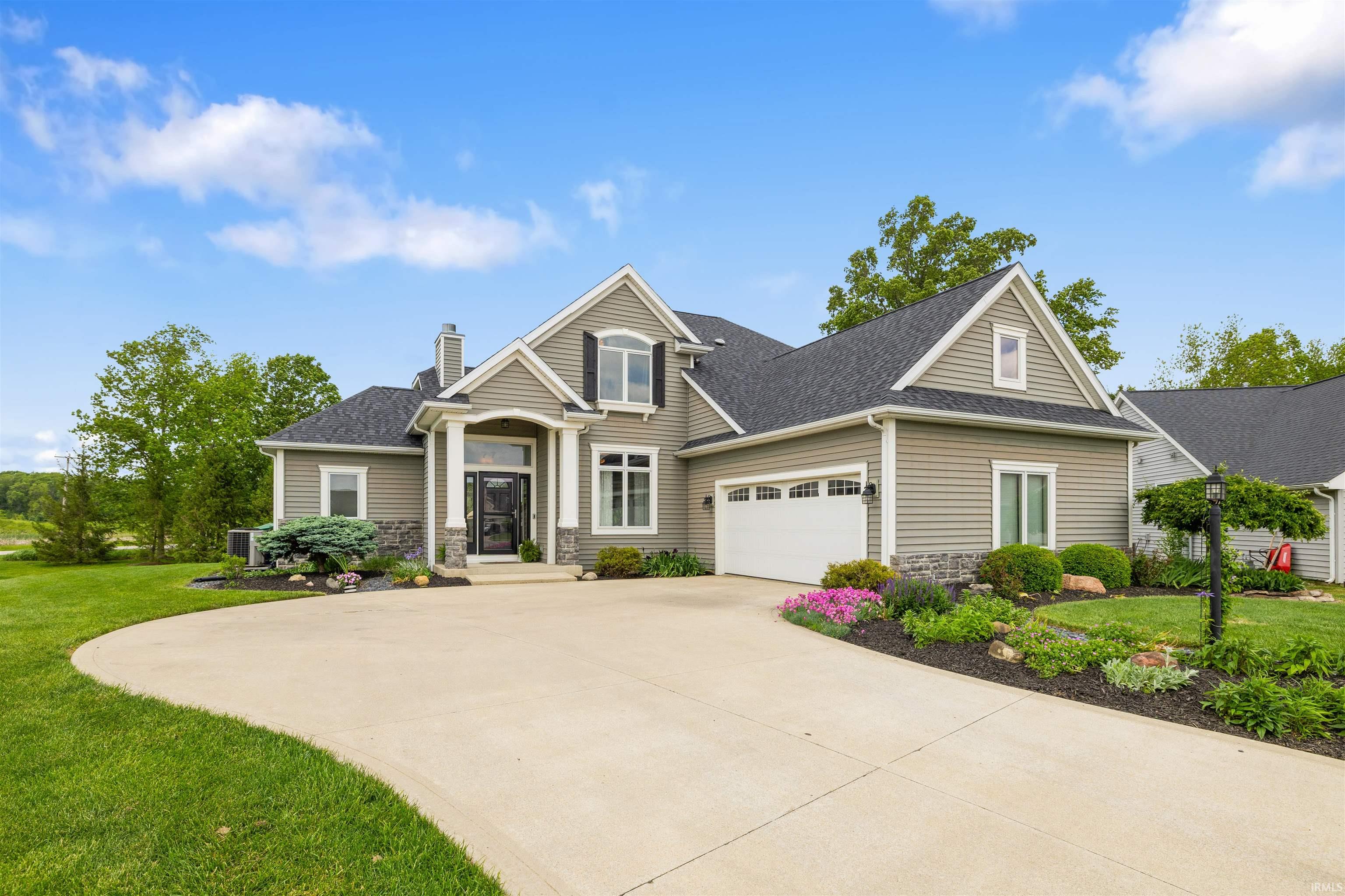 Siding facade with stone accents, a multi-car driveway, attached garage, and mature landscaping