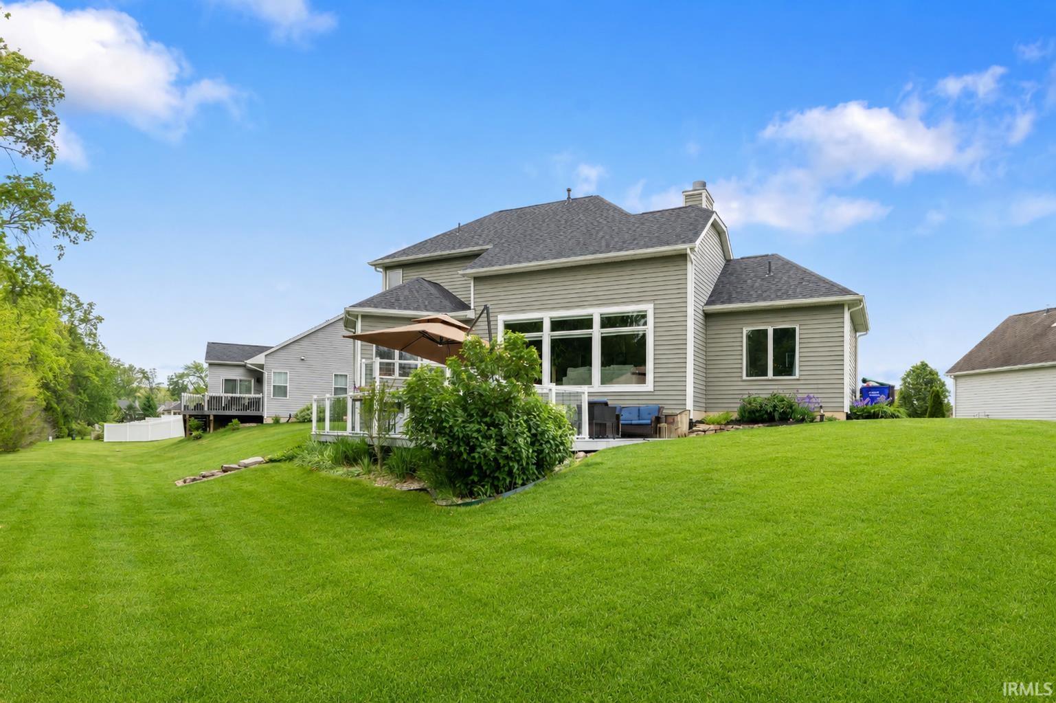 Expansive rear yard featuring a large green lawn, a multi-level deck with glass panel railing, and a stone patio