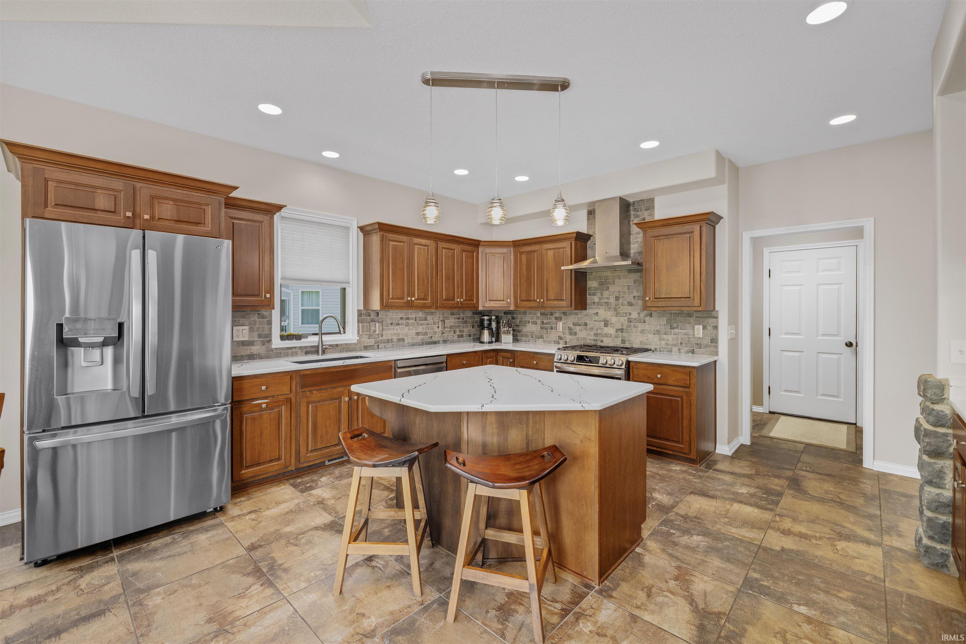 Kitchen featuring a hexagonal island with a light-toned countertop, stainless steel appliances, wood cabinetry, stone tile backsplash, and recessed lighting