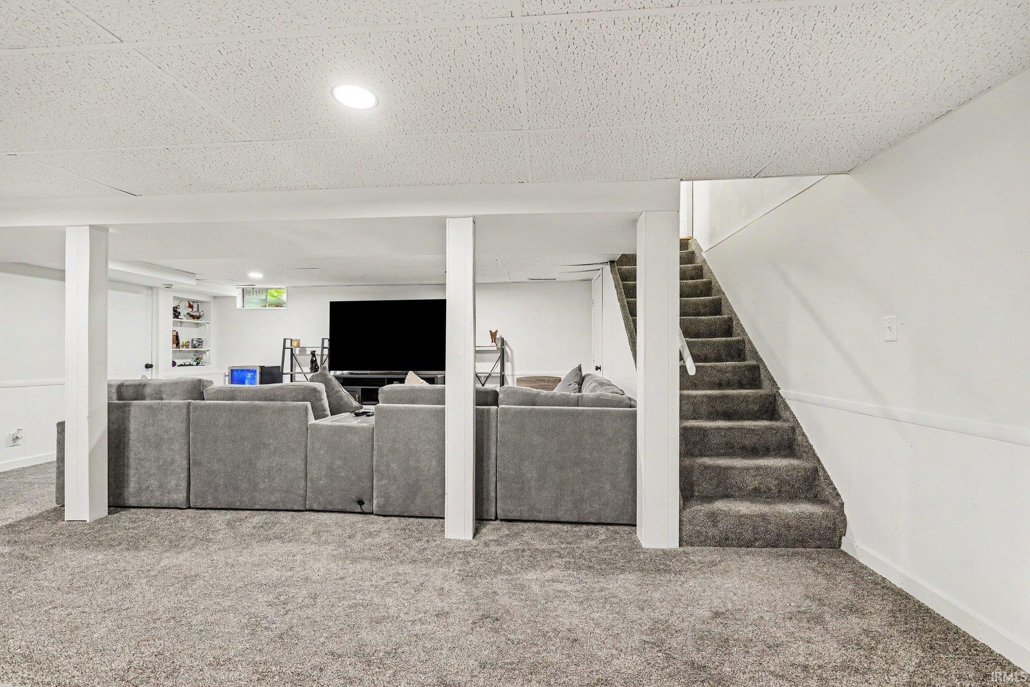Finished lower level featuring recessed lighting, a carpeted staircase, white support columns, and white walls with wainscoting