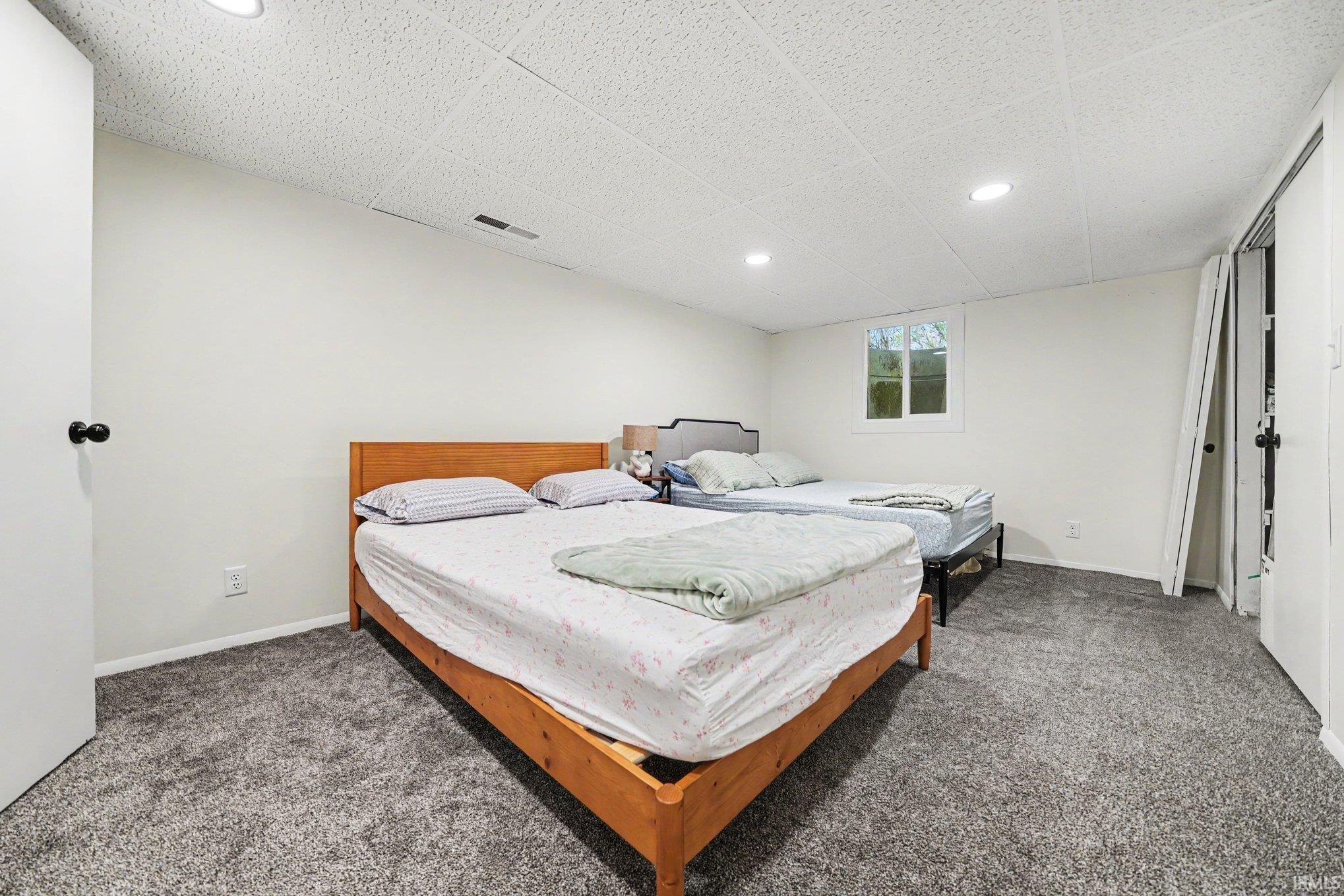 Spacious room featuring neutral carpeting, white walls, recessed lighting, and a drop ceiling