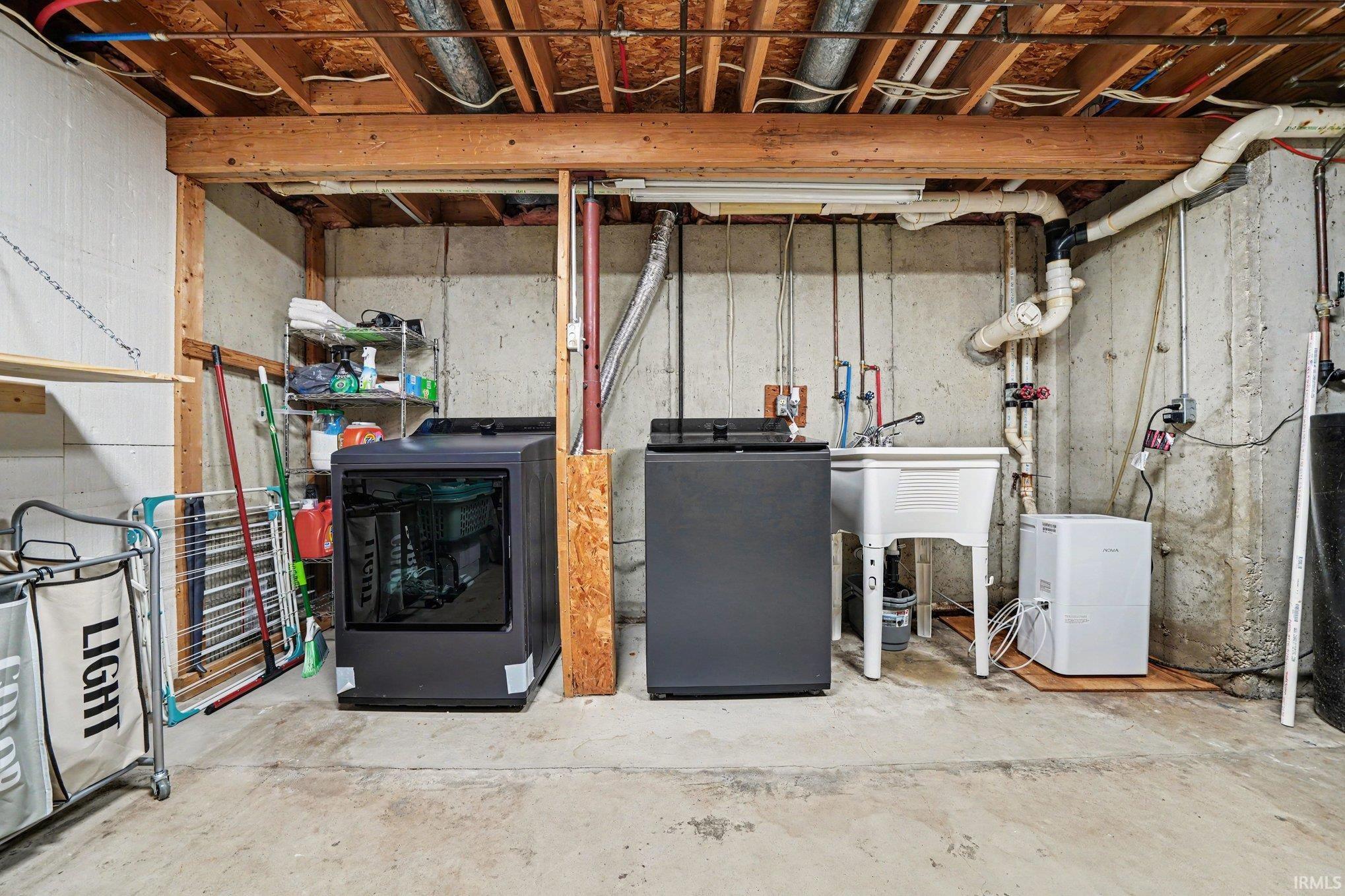 Dedicated laundry area featuring a utility sink, concrete flooring, exposed ceiling joists, and visible plumbing