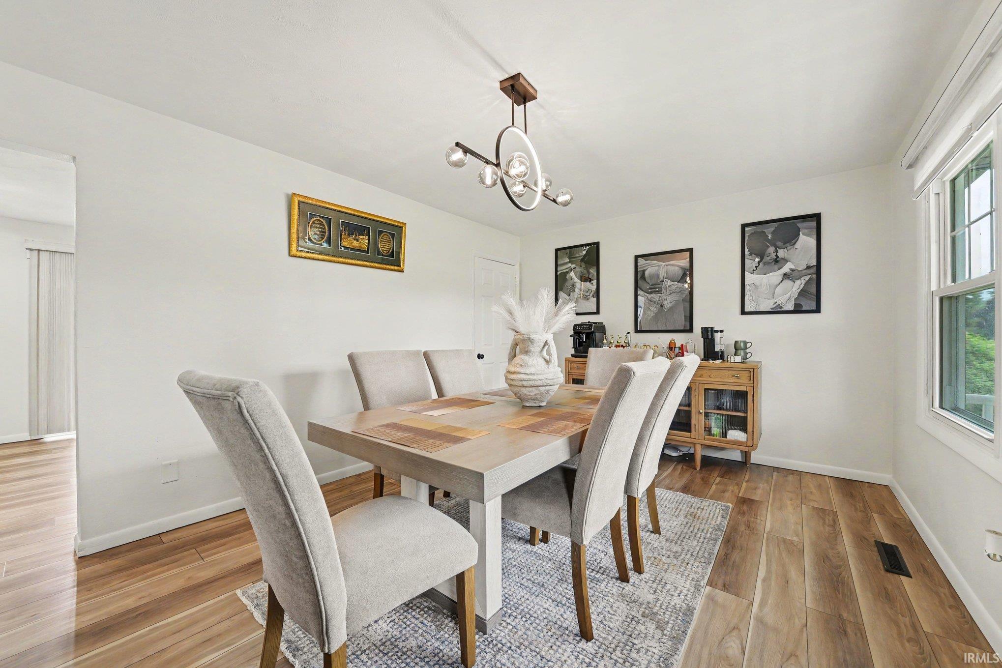 Dining area featuring wood-finish flooring, a modern linear chandelier, and a large window with natural light