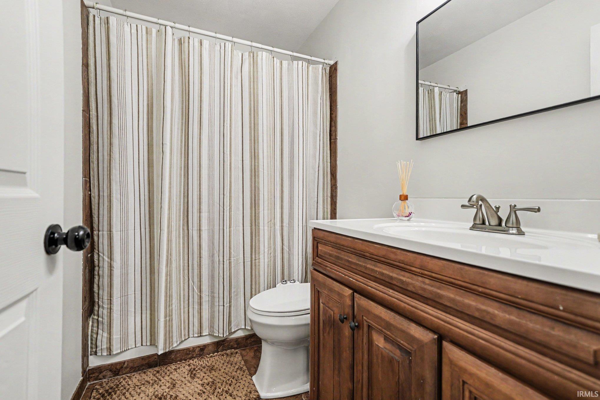 Bathroom featuring a wood-finish vanity with a white countertop and integrated sink, brushed nickel faucet, and a wall-mounted rectangular mirror
