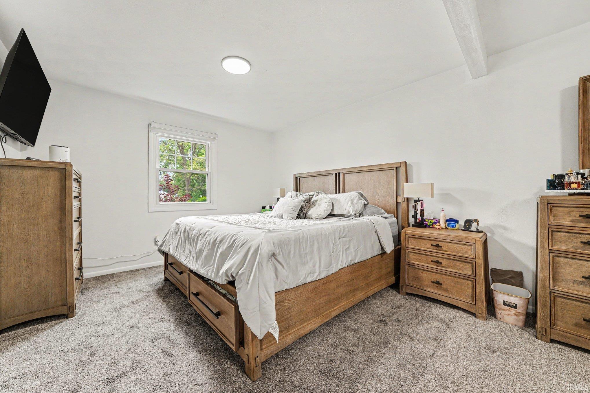Bedroom featuring a window with exterior tree scenery, recessed ceiling lighting, a textured carpet, and a visible ceiling beam