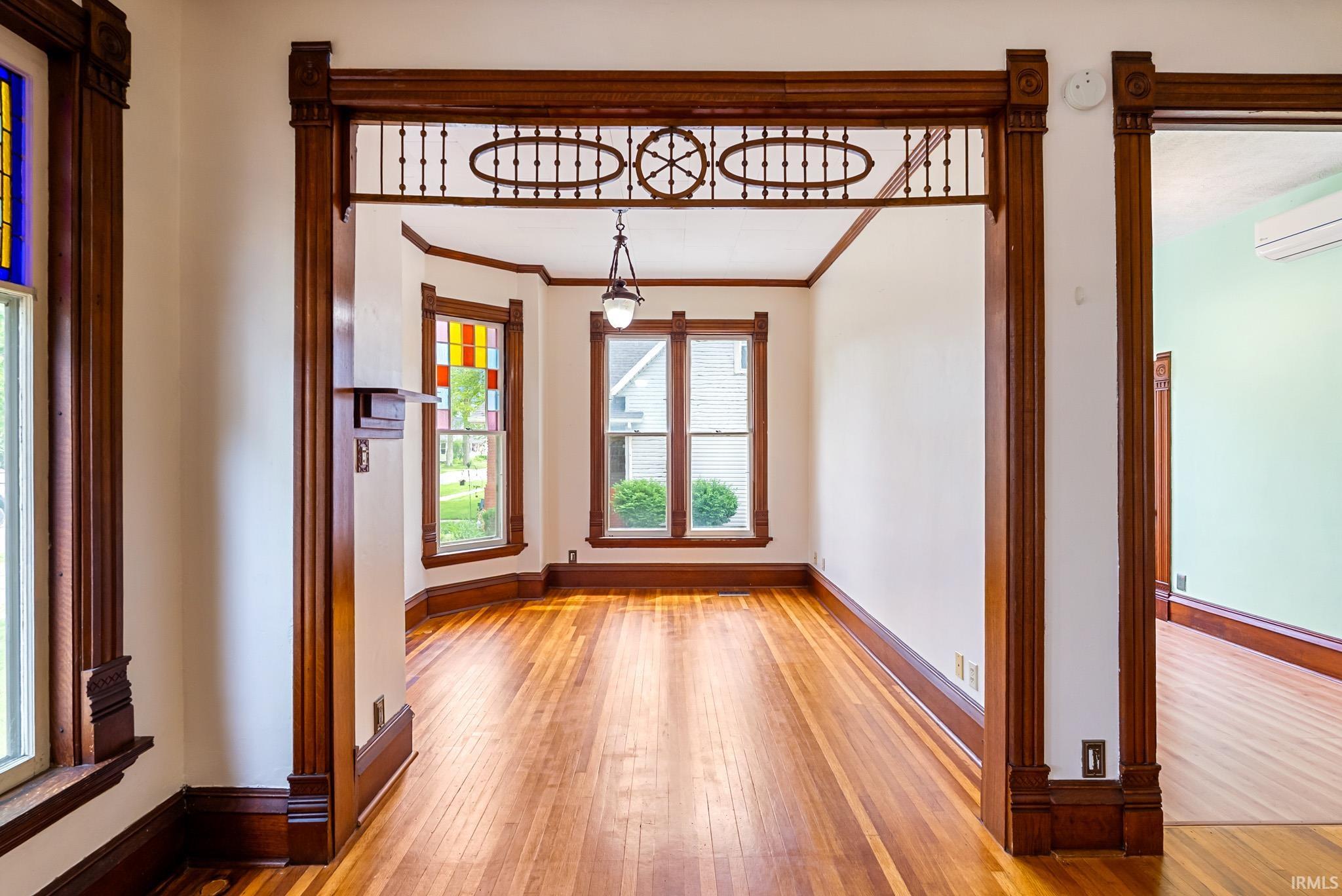 Interior space featuring rich wood trim, ornate archway detailing, wood-finish flooring, bay windows, and a pendant light fixture