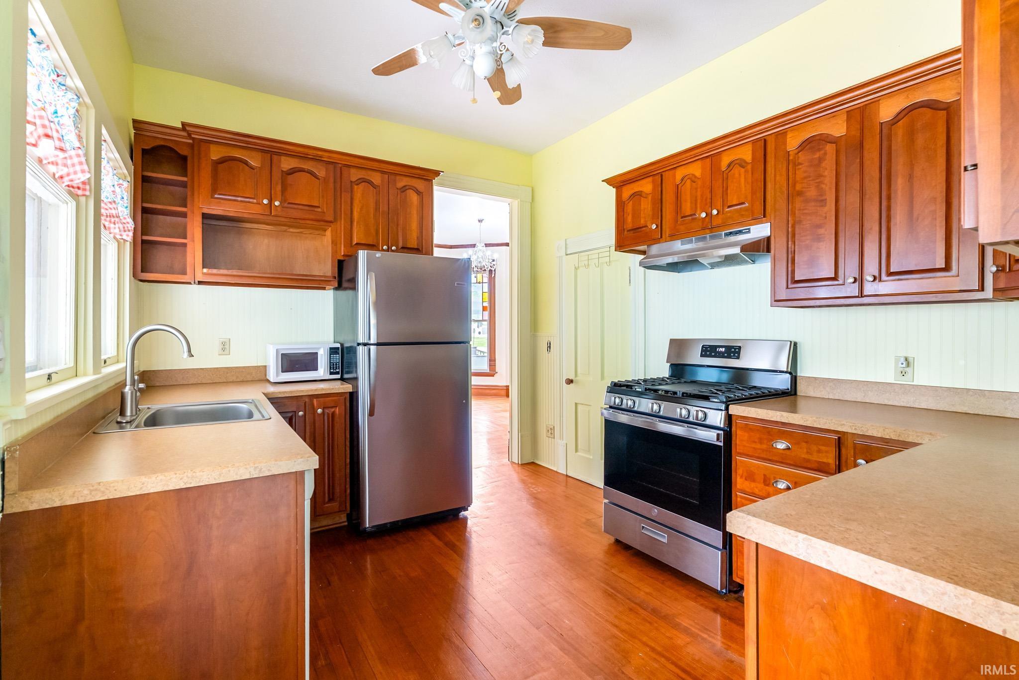 Kitchen featuring wood-finish flooring, warm-toned cabinetry, light-colored countertops, stainless steel appliances, and a ceiling fan