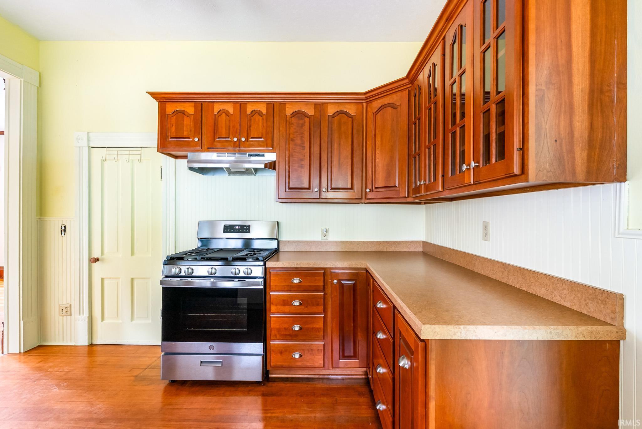 Kitchen featuring wood-finish flooring, rich wood cabinetry, stainless steel range with overhead hood, and ample countertop space