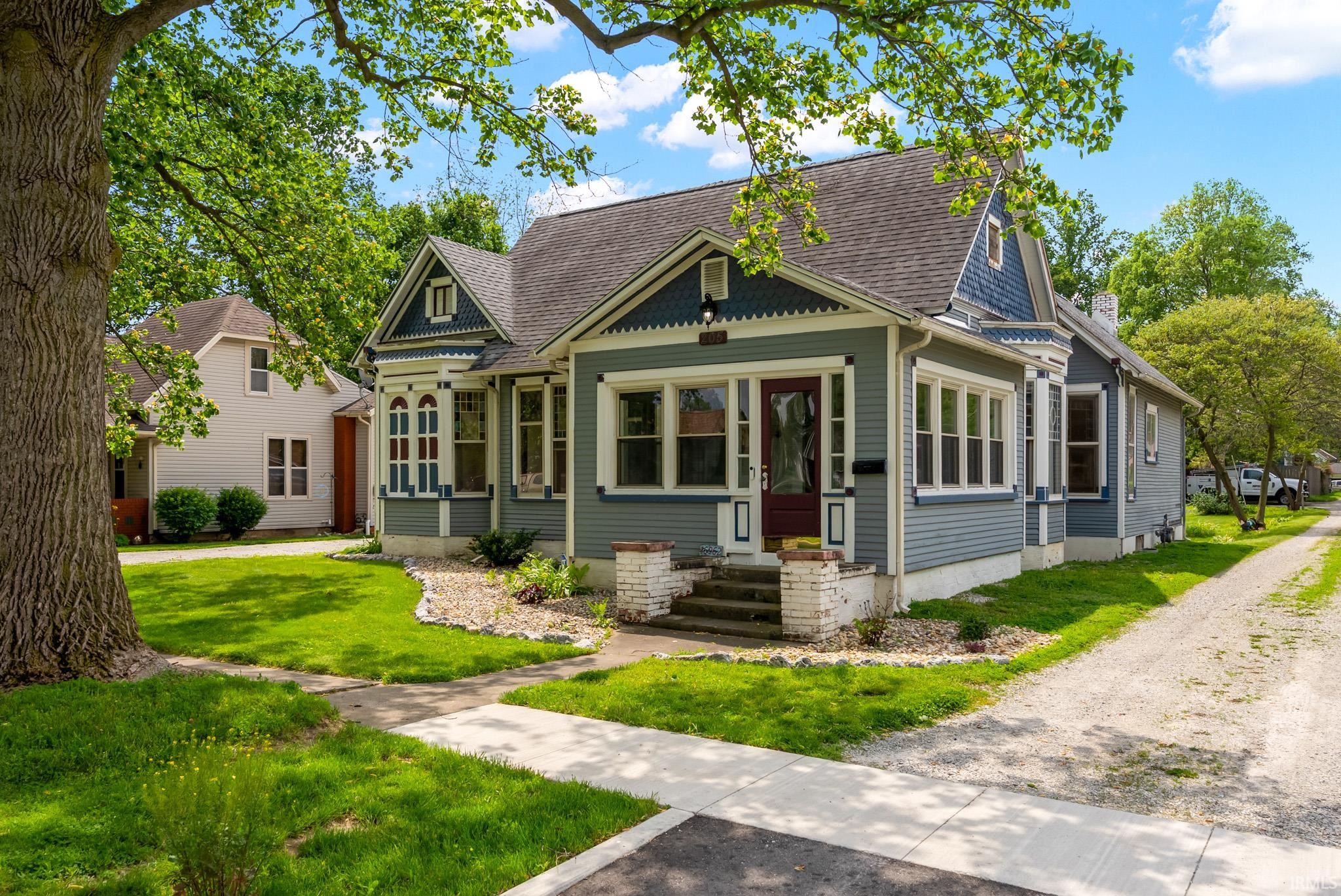 Victorian-style residence featuring a prominent gable with decorative trim, horizontal siding, a covered porch, a crimson entry door, and multiple bay windows