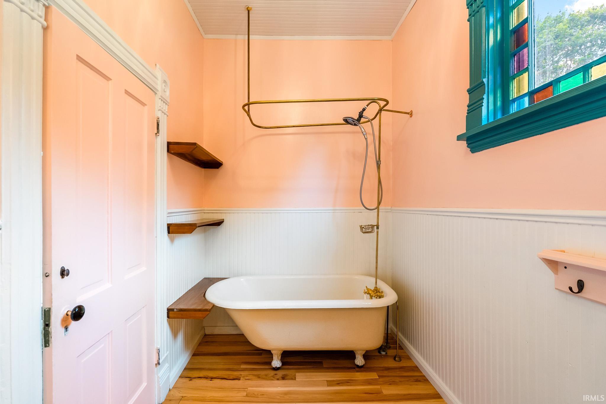 Bathroom featuring a clawfoot tub with a brass shower fixture, wood-finish flooring, and wainscoting