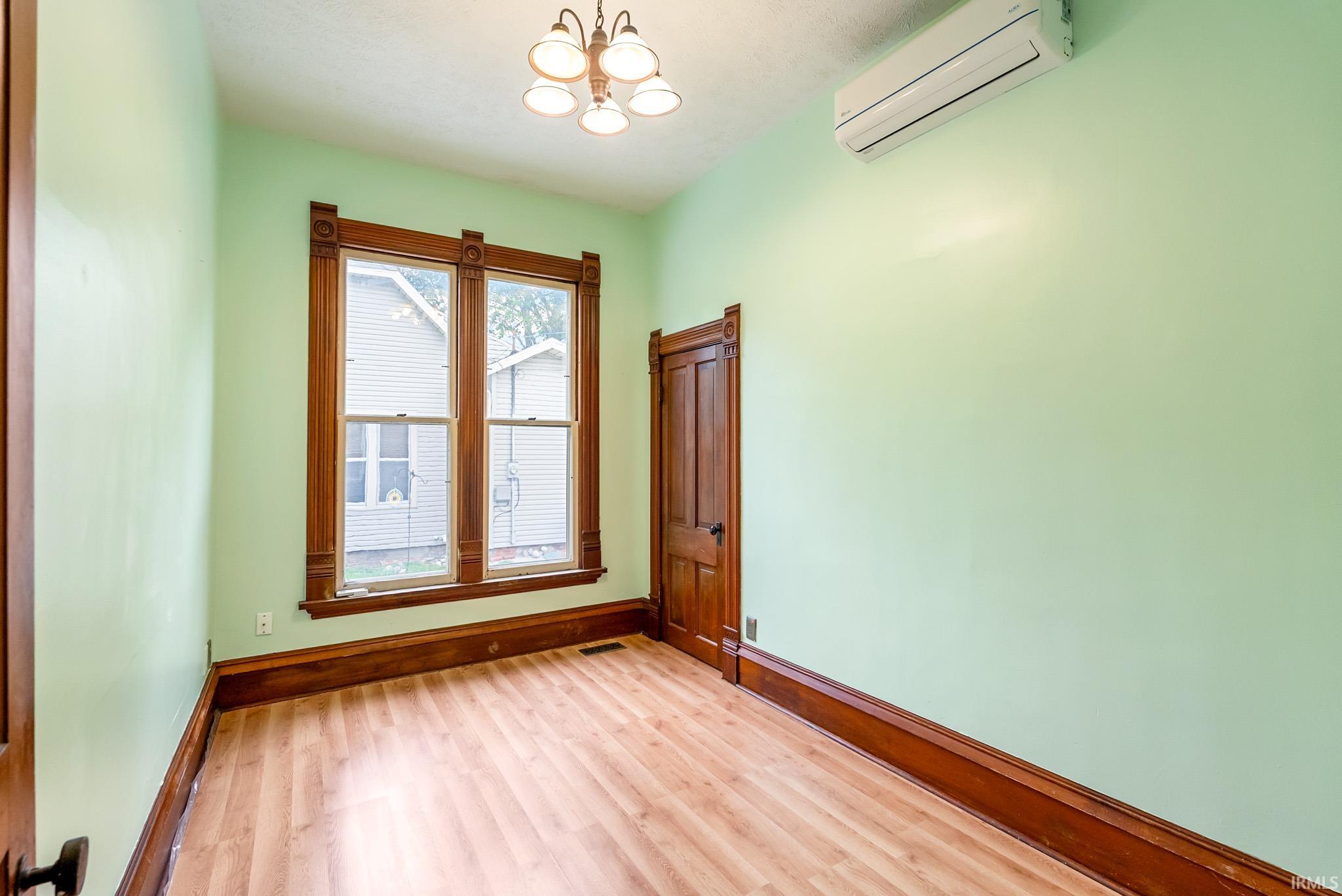 Room with wood-finish flooring, two large sash windows with ornate wood trim, and a built-in mini-split HVAC unit