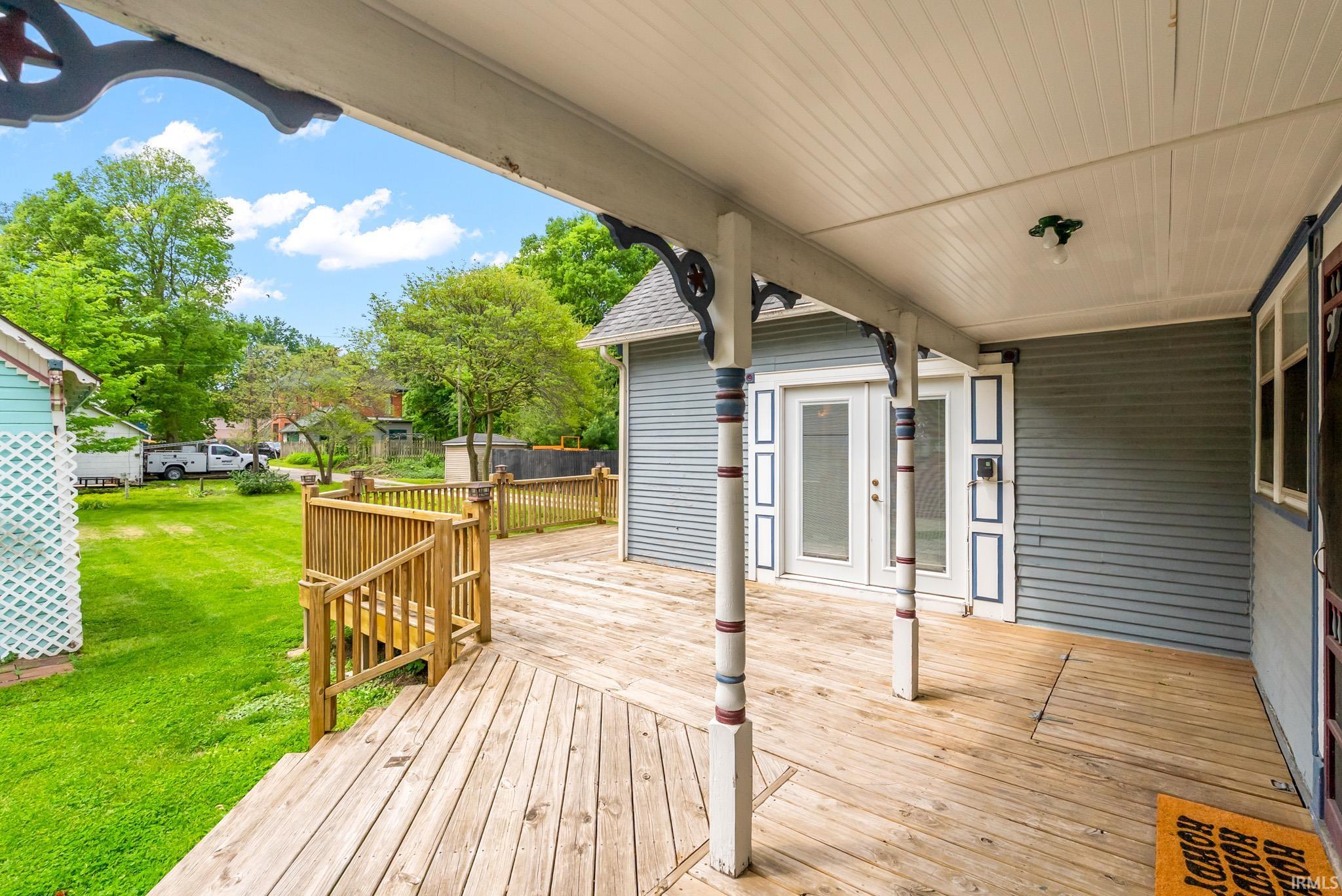 Expansive wooden deck with railing, featuring a covered porch with decorative support columns and a beadboard ceiling