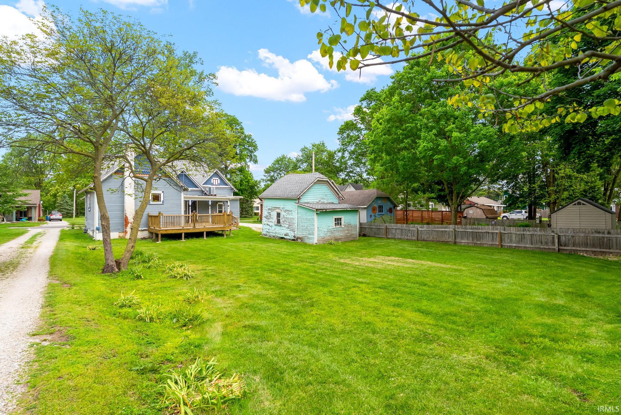 Expansive green lawn with mature trees and a gravel driveway