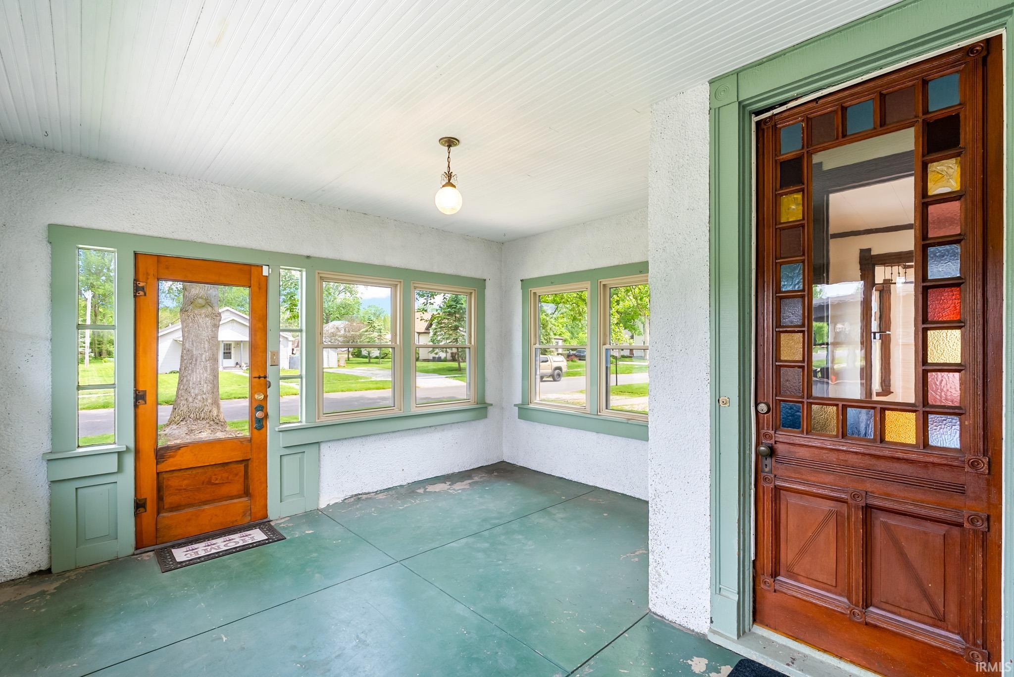 Enclosed porch featuring a stained-glass entry door, multiple windows, beadboard ceiling, and a concrete floor
