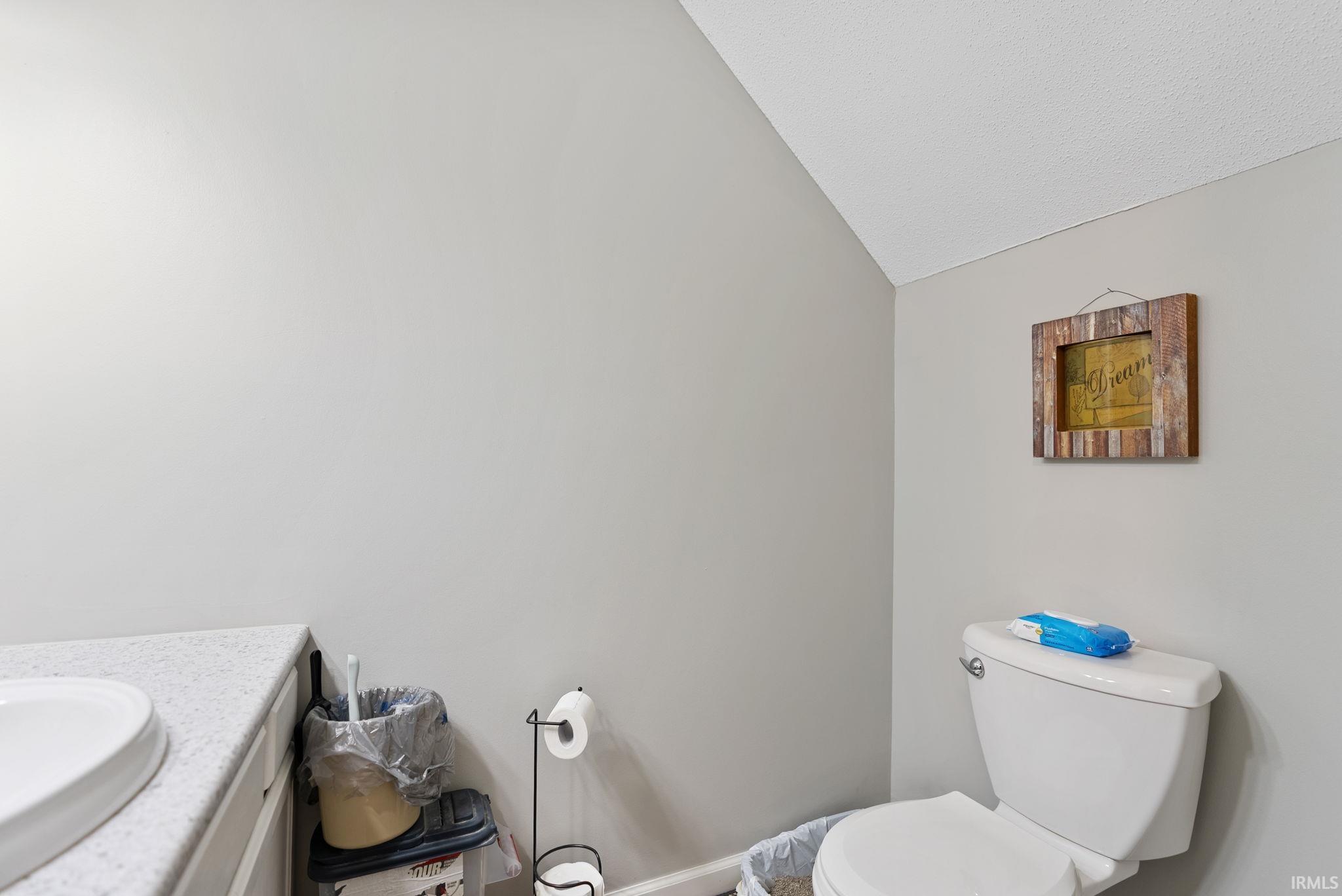 Powder room featuring a white toilet, light gray walls, and an angled ceiling