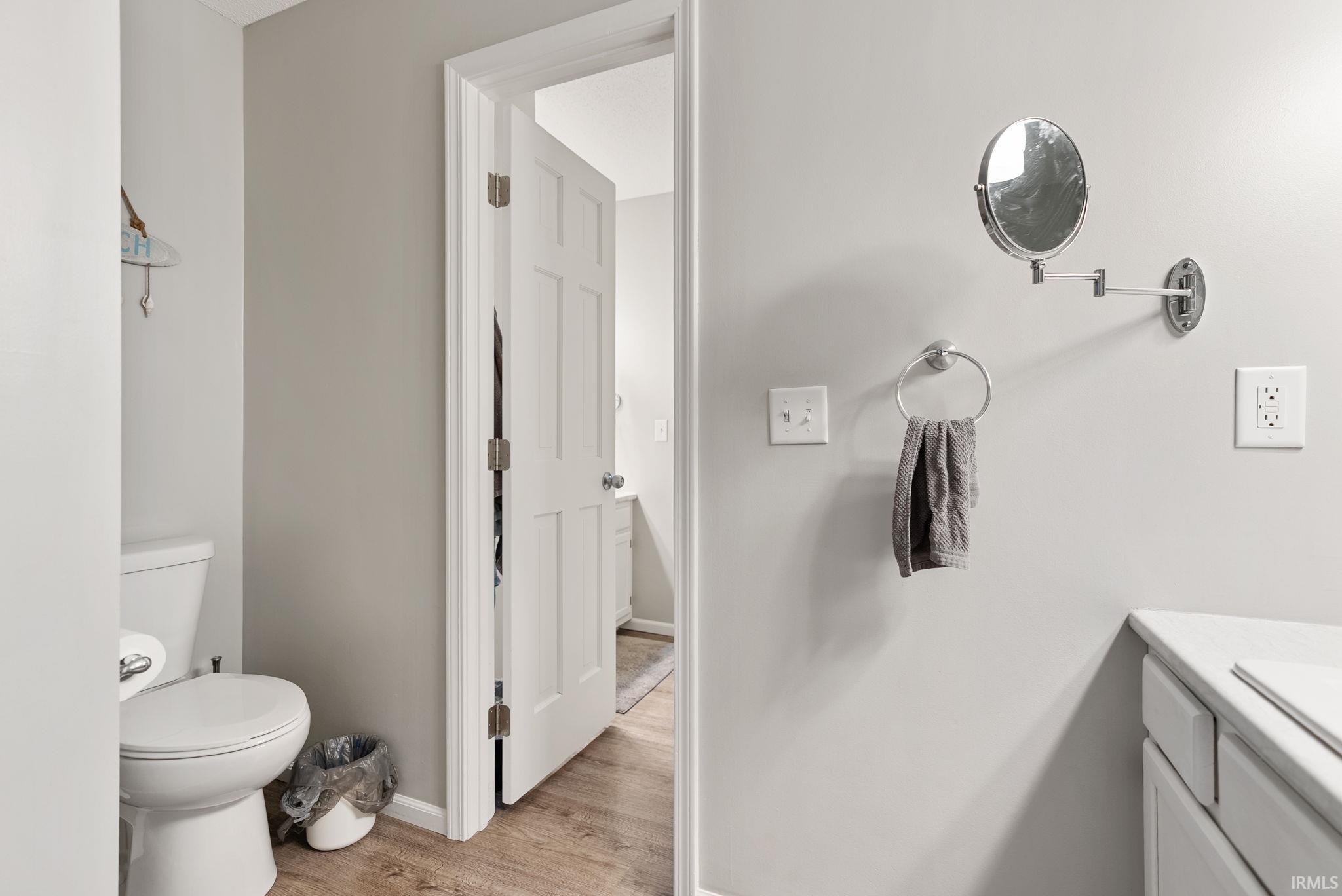 Bathroom featuring a white toilet, light-toned walls, wood-finish flooring, and a white paneled door