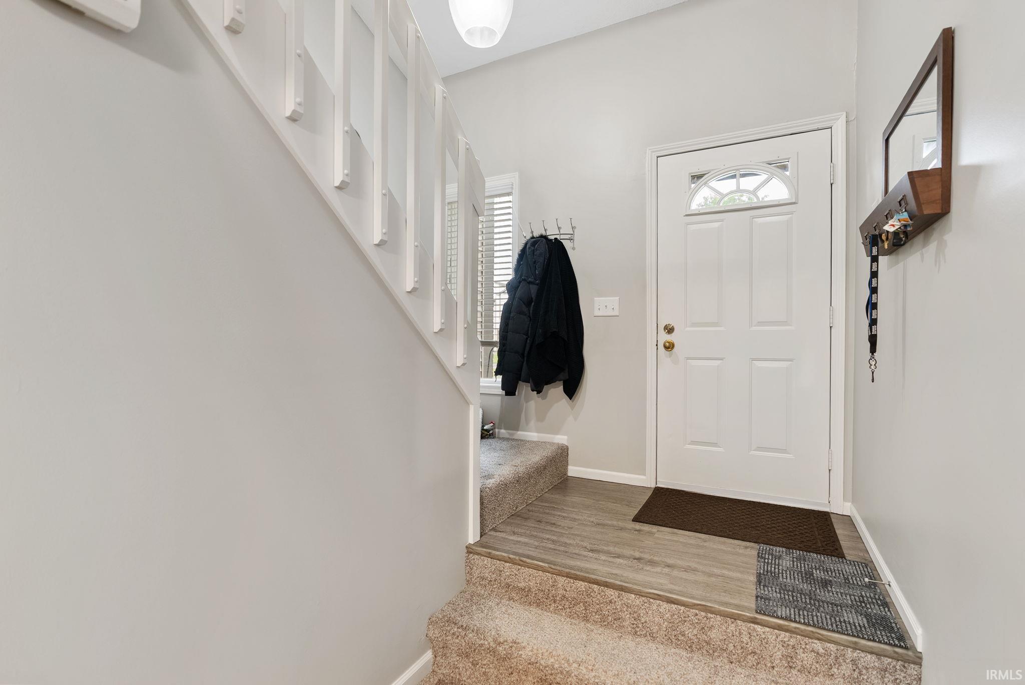 Entryway featuring a white paneled door with an arched glass insert, wood-finish flooring, and a carpeted staircase with white balusters
