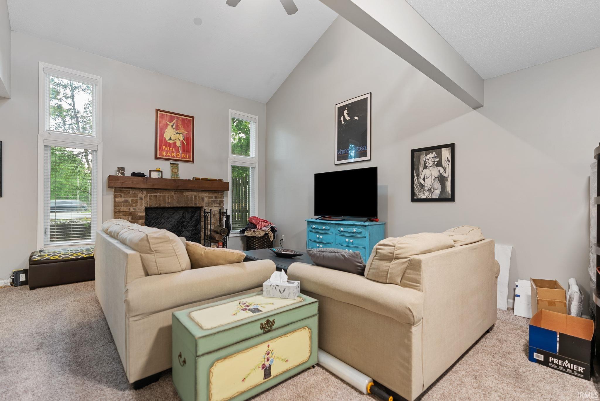 Vaulted ceiling with an exposed beam, brick fireplace, wood mantel, and tall windows