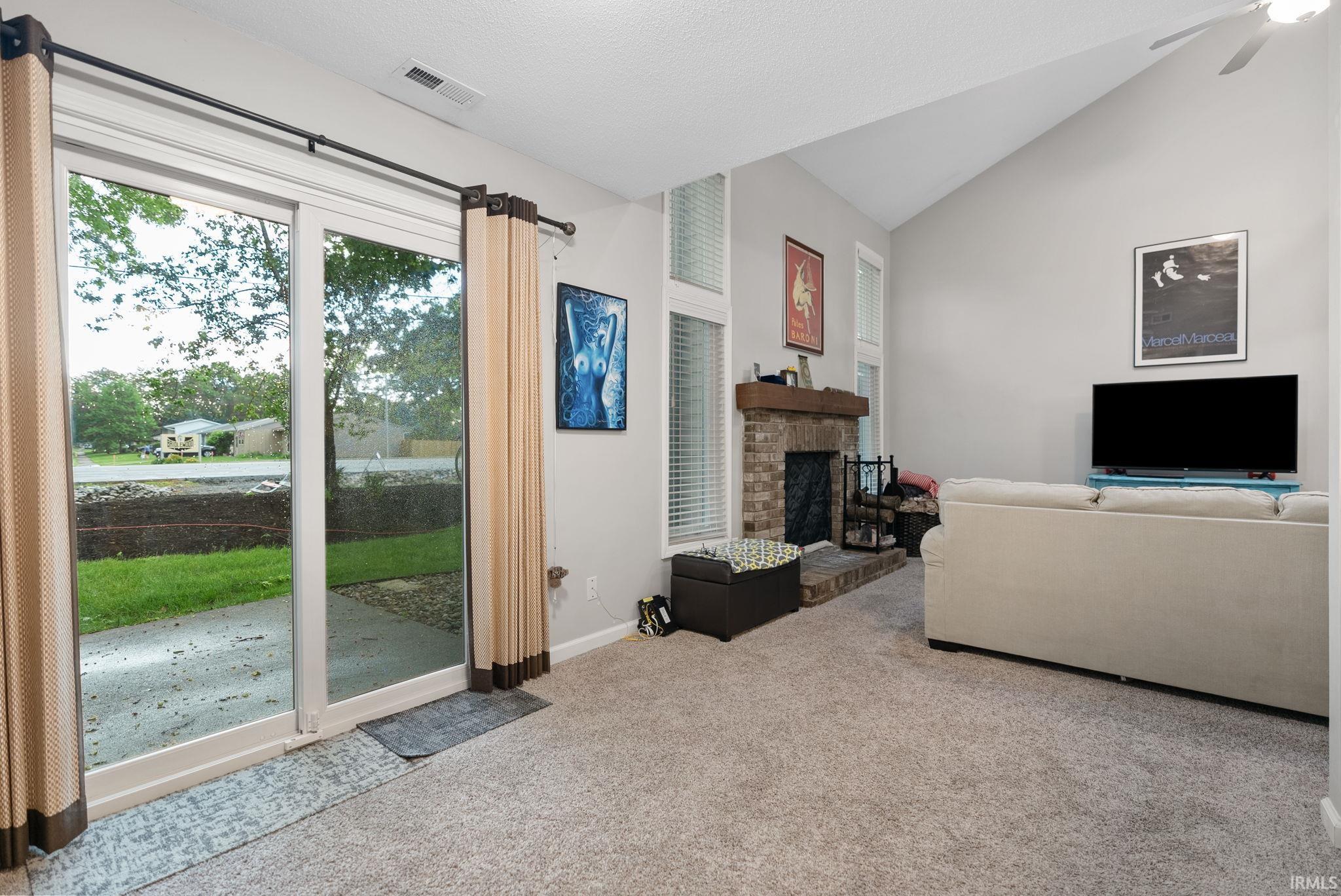 Living area featuring a vaulted ceiling and a stone fireplace with a wood mantel