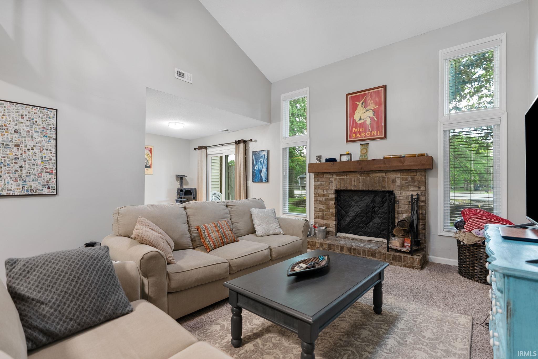 Living area featuring a brick fireplace with a wood mantle, vaulted ceiling, and multiple windows
