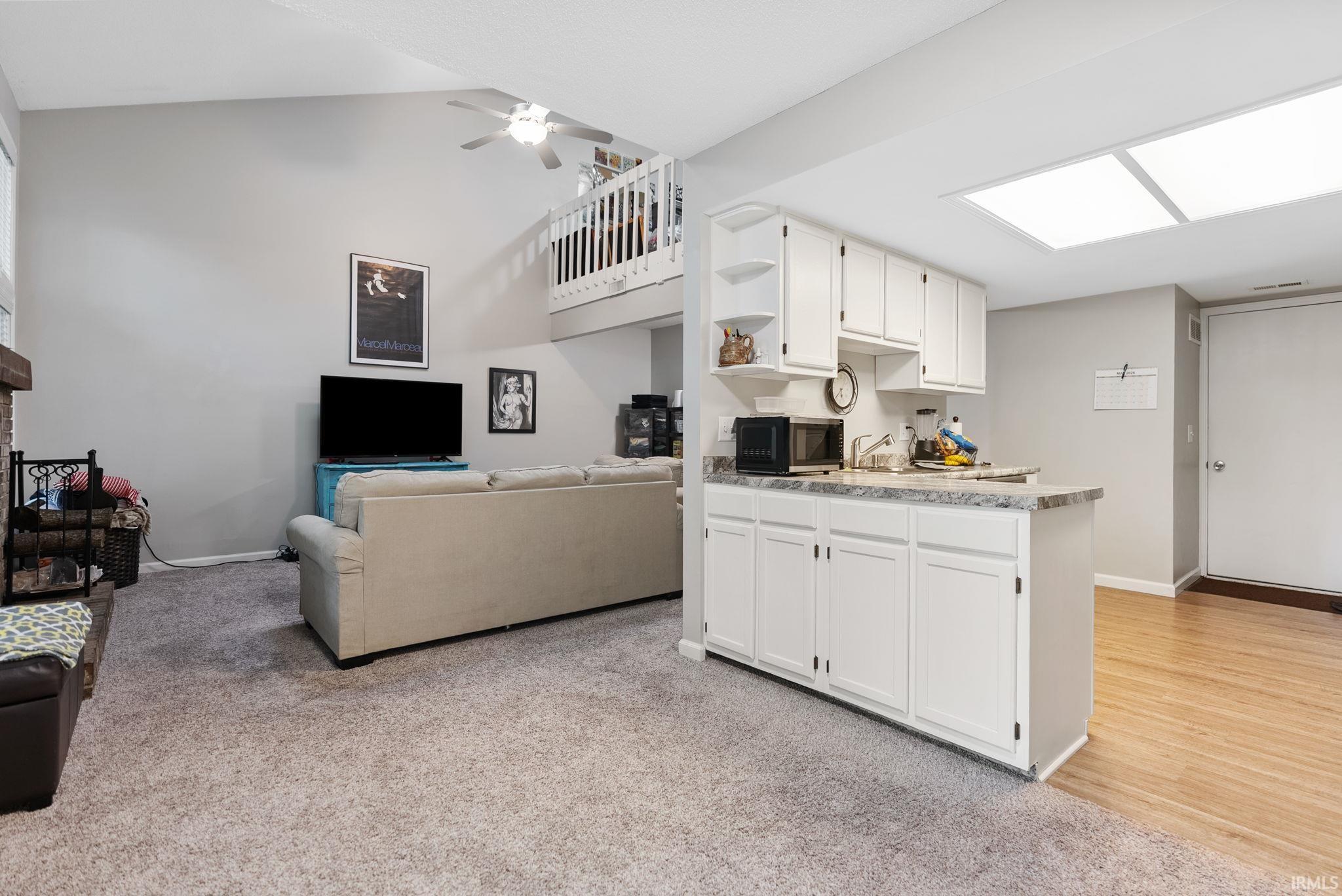 Open-concept living space featuring vaulted ceilings, a ceiling fan, and a functional wet bar with white cabinetry