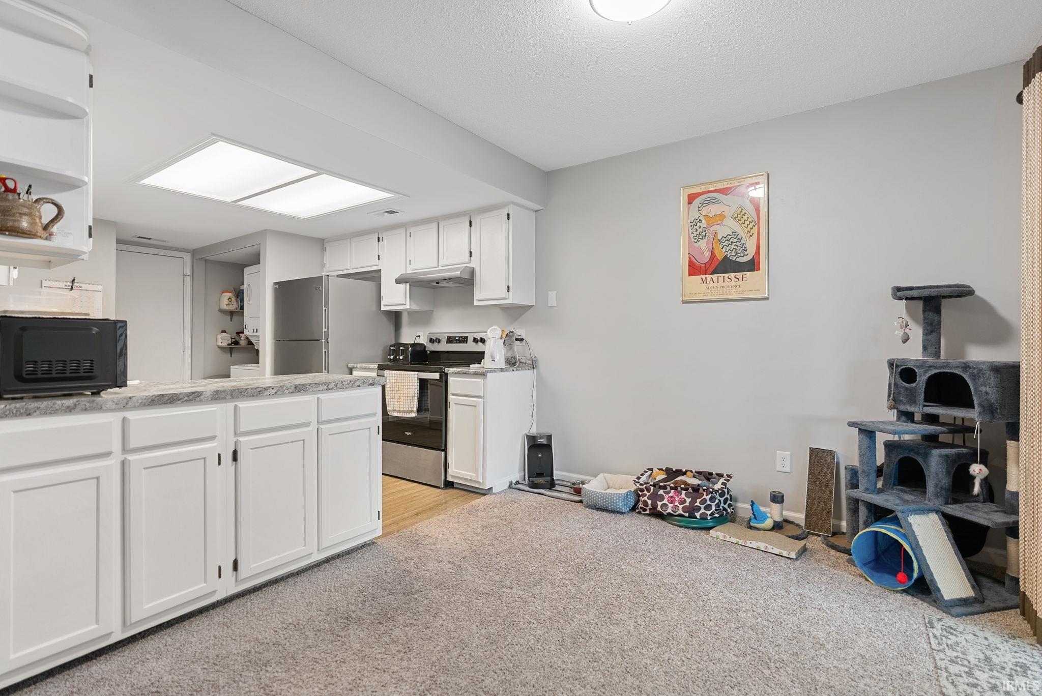 Kitchen featuring white cabinetry, stainless steel appliances, a bar-height counter, a large overhead light fixture, and wood-finish flooring