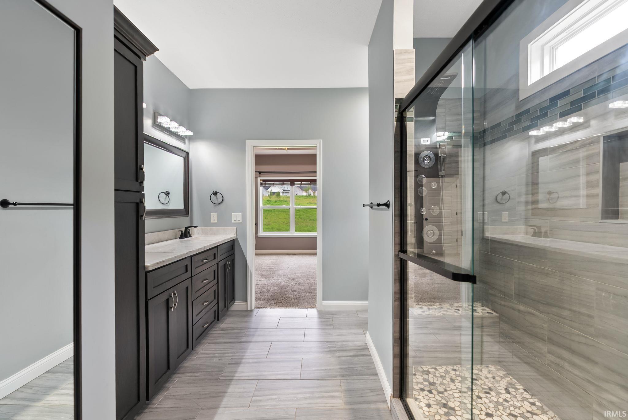 Bathroom featuring a glass-enclosed shower with pebble flooring and tiled walls, a dark wood-finish vanity with a light countertop, and wood-finish flooring