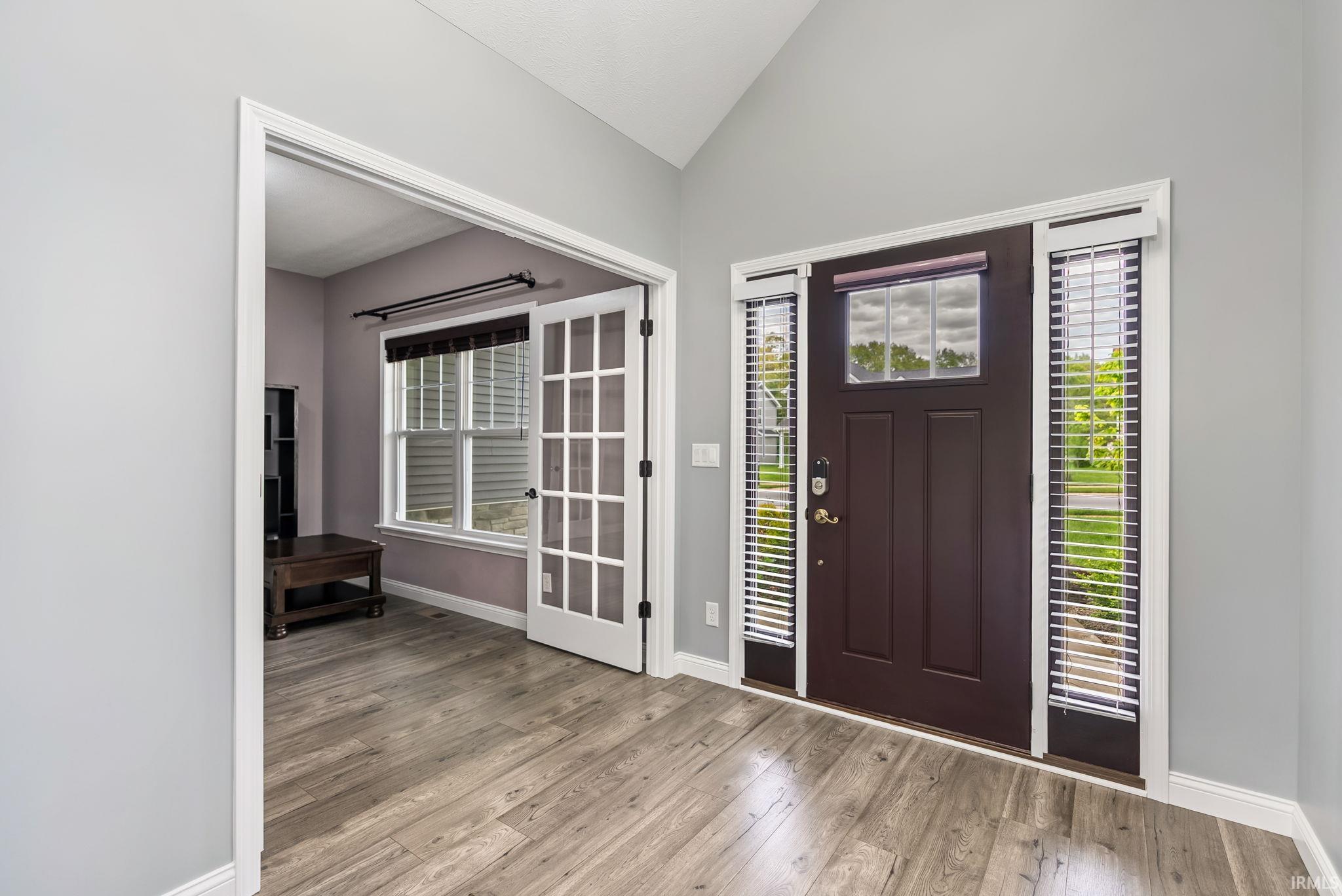 Entryway featuring wood-finish flooring, a dark-stained front door with sidelights and transom window, and a vaulted ceiling