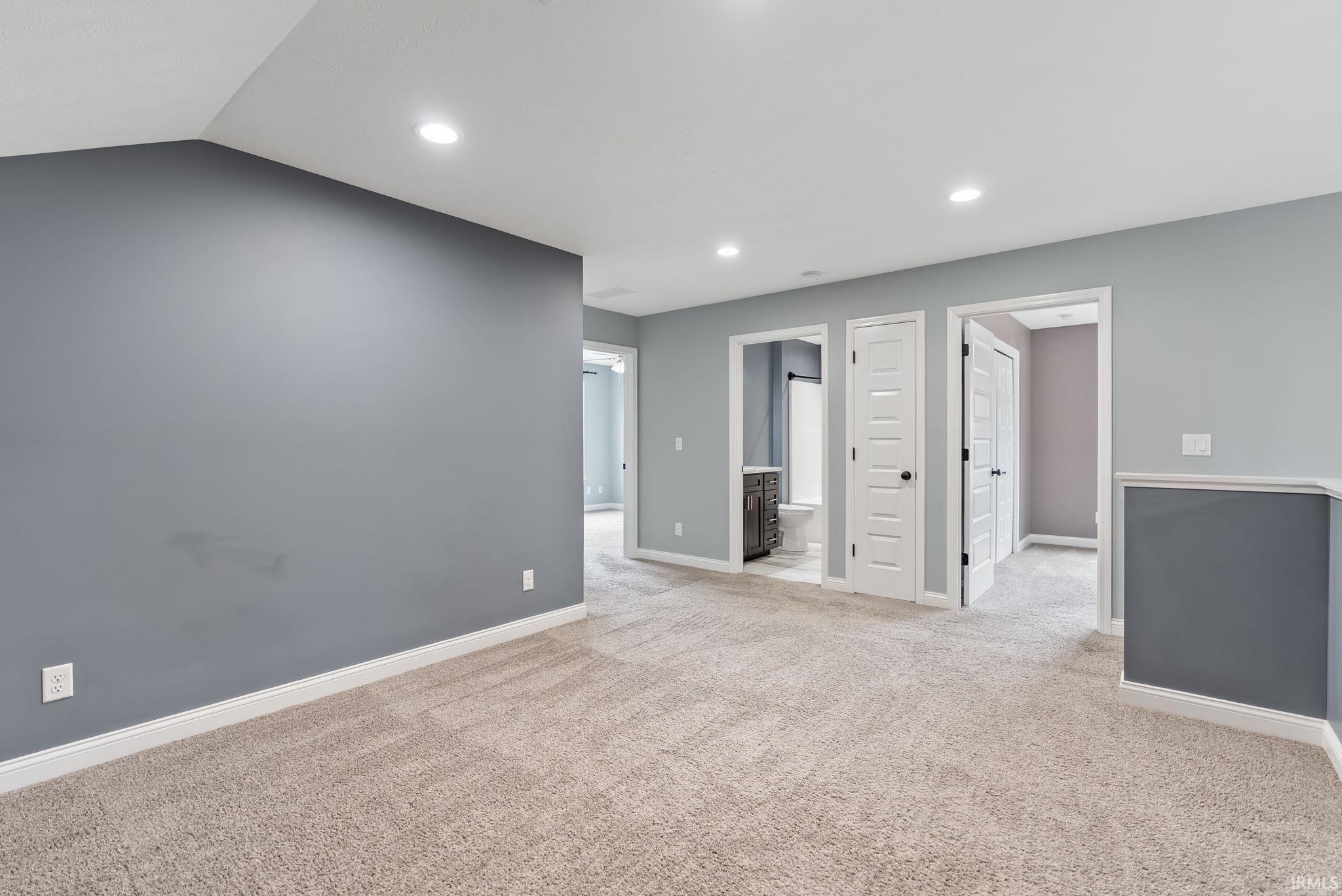 Spacious room featuring neutral carpeting, recessed lighting, white baseboards, and multiple doorways