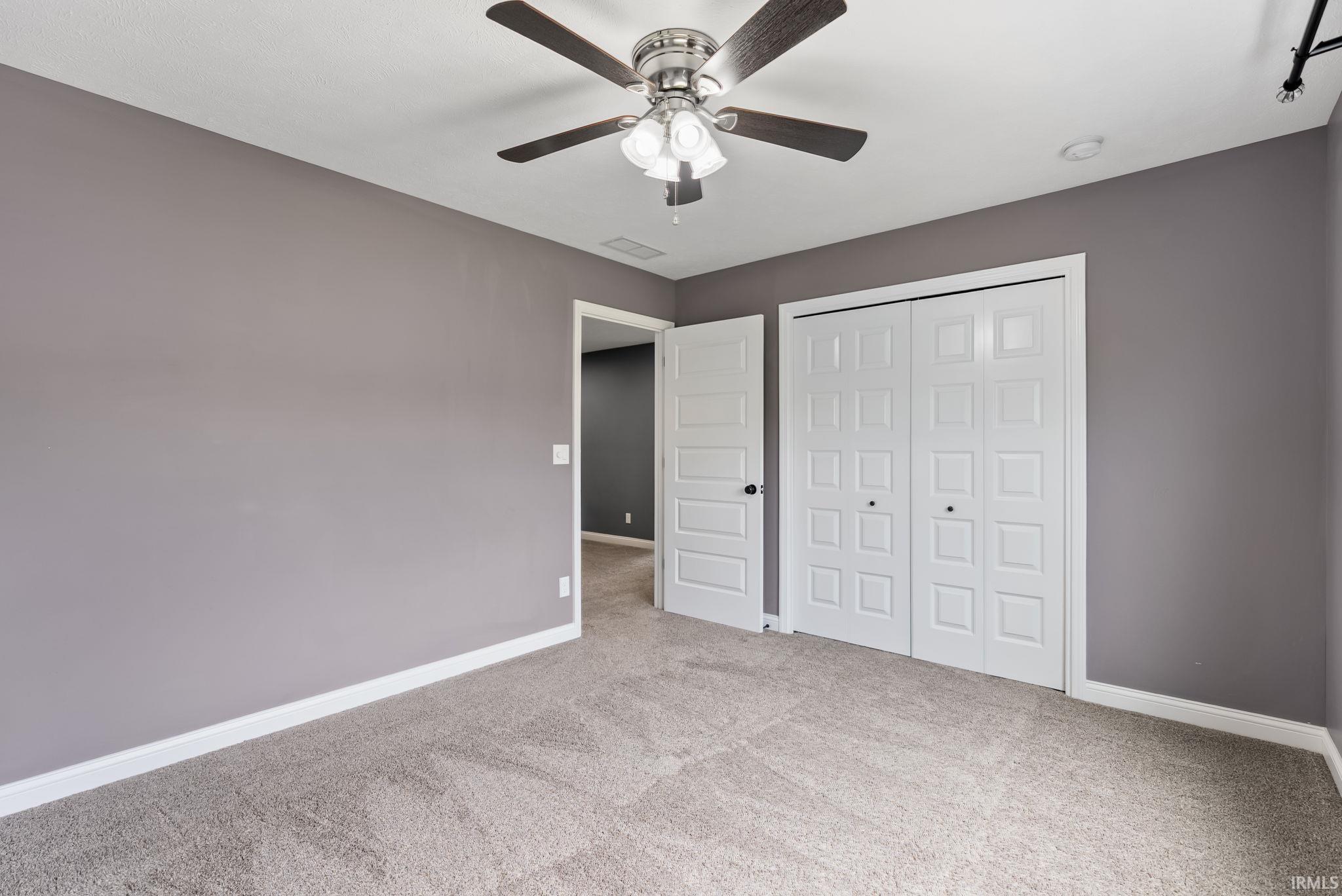 Carpeted room featuring gray walls, white trim, a ceiling fan with light fixture, and bifold closet doors