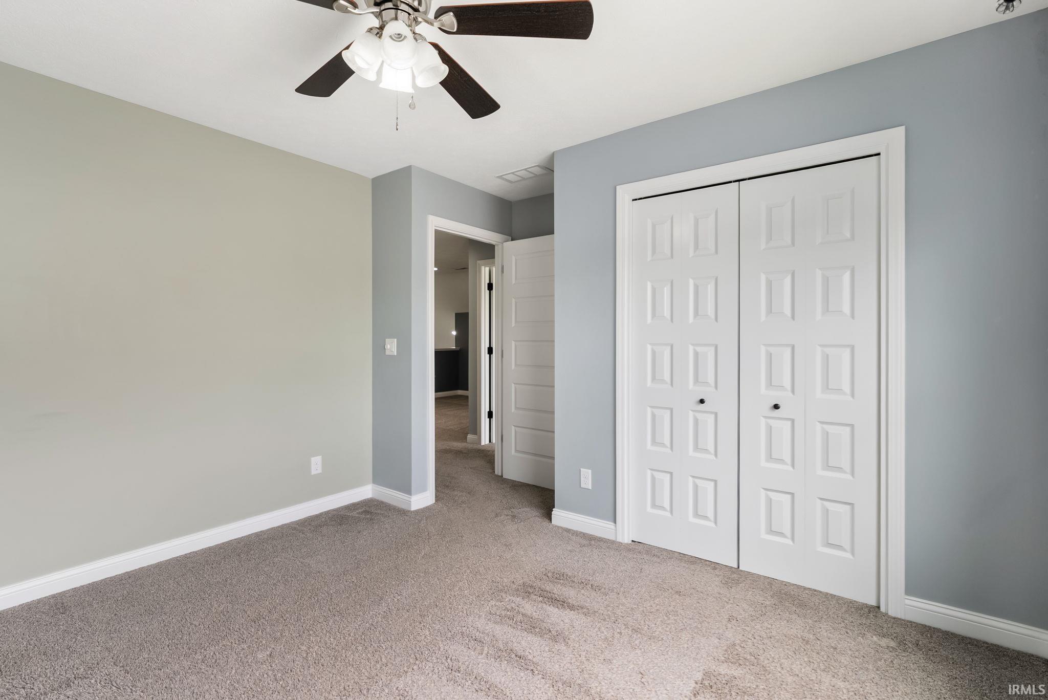Carpeted room with a ceiling fan, bifold closet doors, and contrasting wall colors