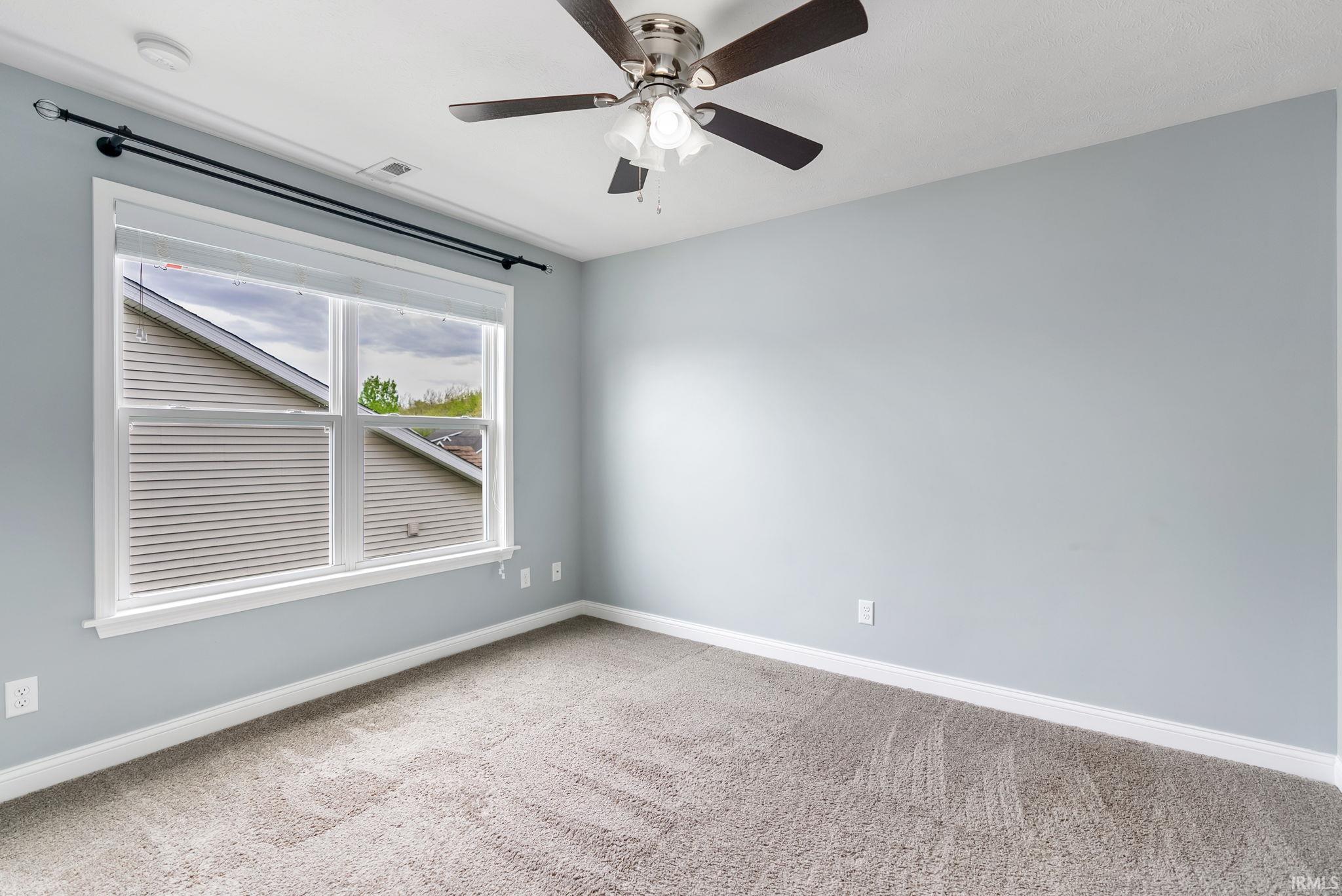 Room featuring light blue walls, gray carpet, a ceiling fan with light fixture, and a white-trimmed window