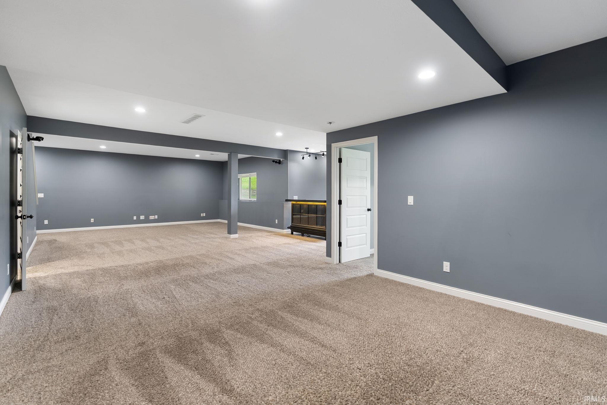 Expansive carpeted room featuring gray walls, white trim, recessed lighting, and a built-in wet bar with dark cabinetry