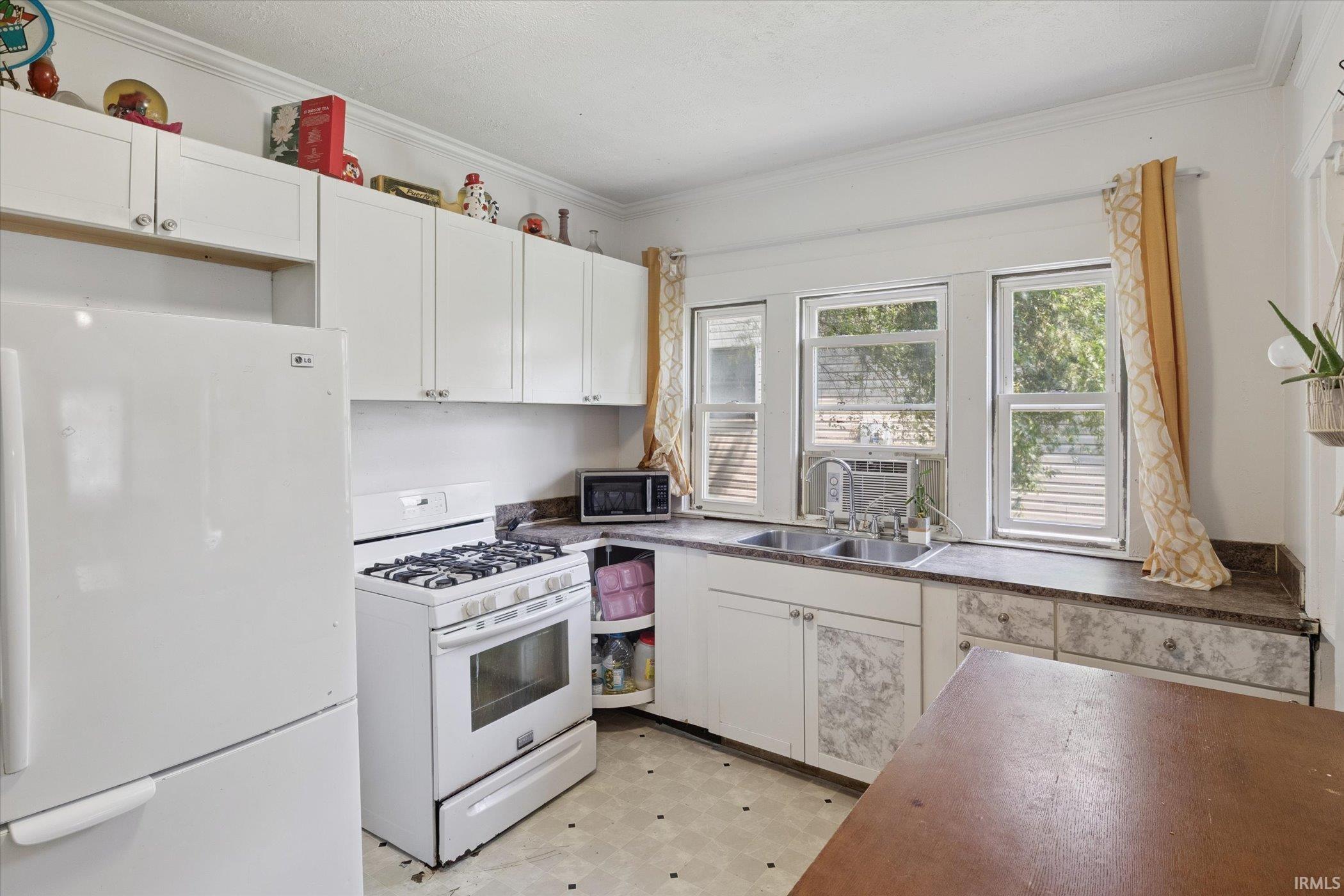 Bright kitchen featuring ample white cabinetry, a double basin sink, and a gas range