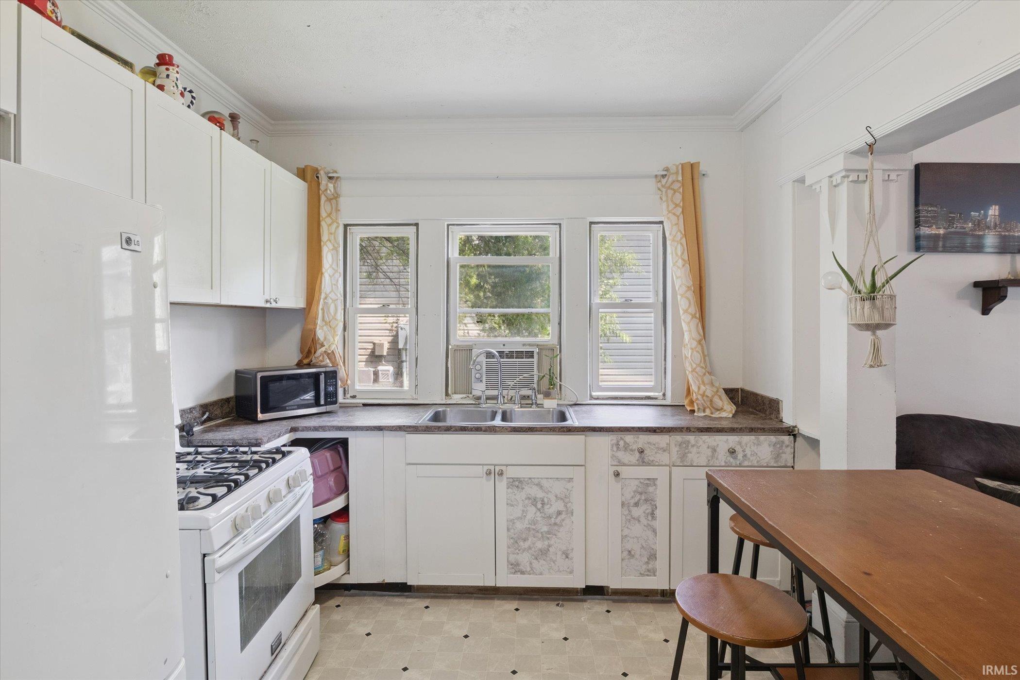 Kitchen space featuring white cabinetry, a double basin sink, and a gas range