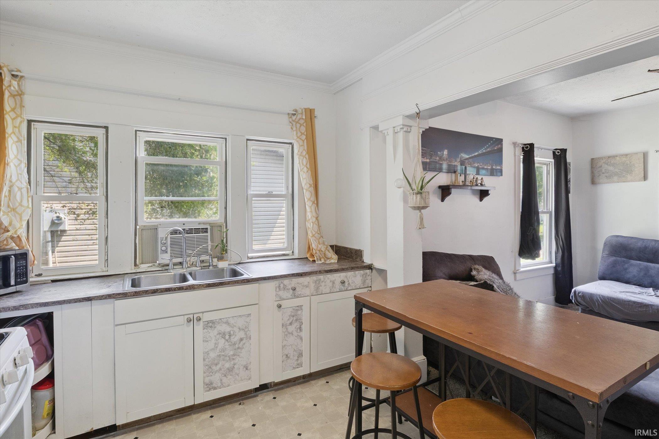 Kitchen with white cabinetry, a double basin sink, and a countertop extending beneath three windows