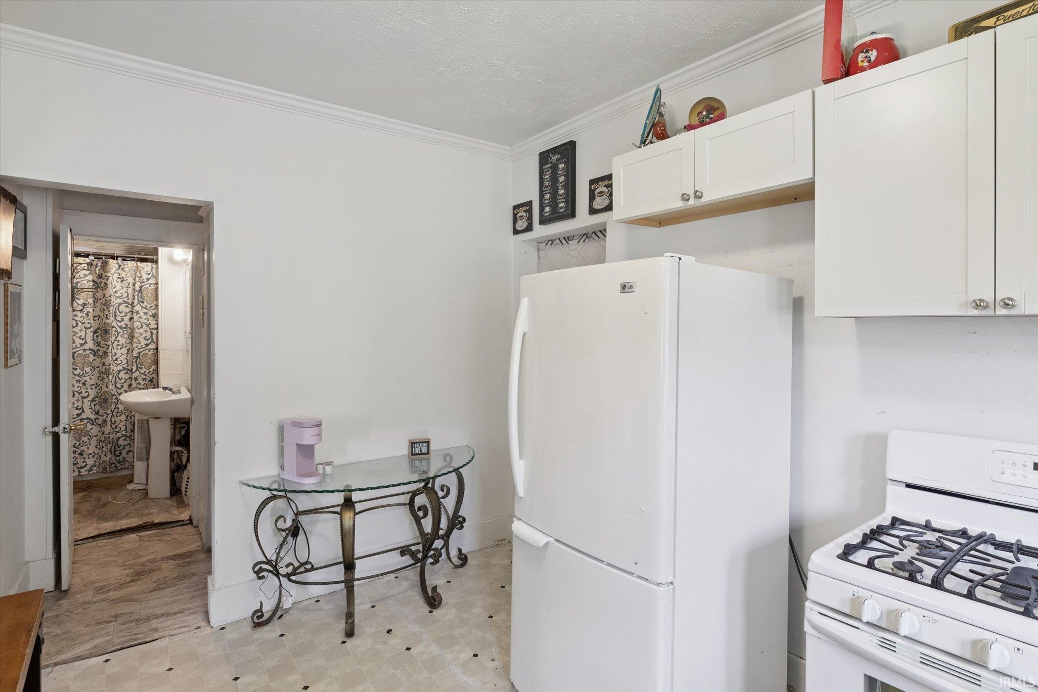 White kitchen featuring a gas range, white cabinetry, and crown molding