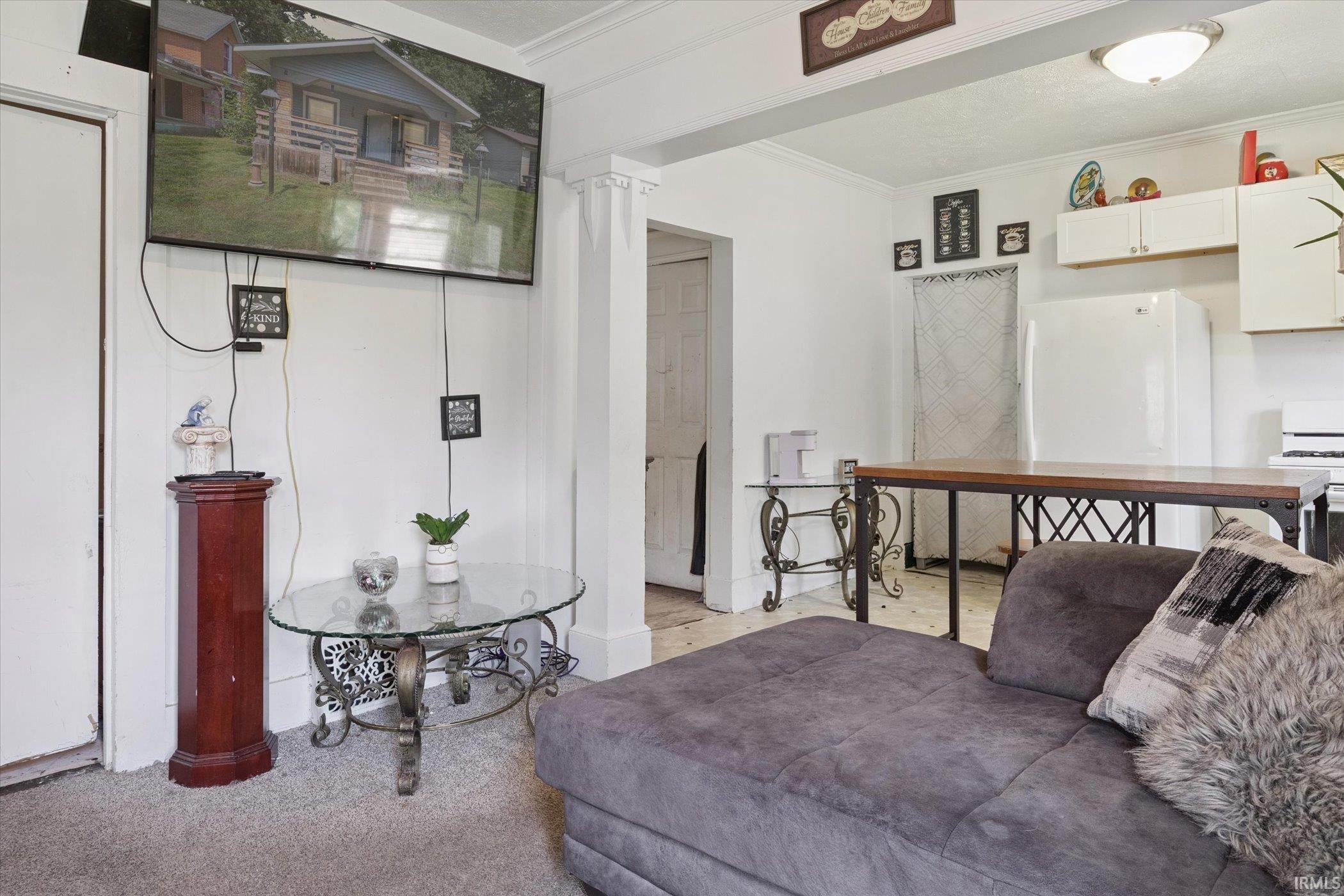 White wall paneling with decorative trim, carpeted flooring, and a kitchen area featuring white upper cabinetry, a white refrigerator, and a freestanding white range
