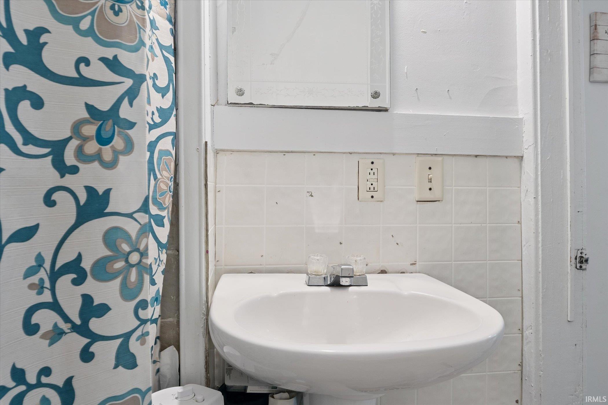 Pedestal sink with chrome faucet set against white tiled walls