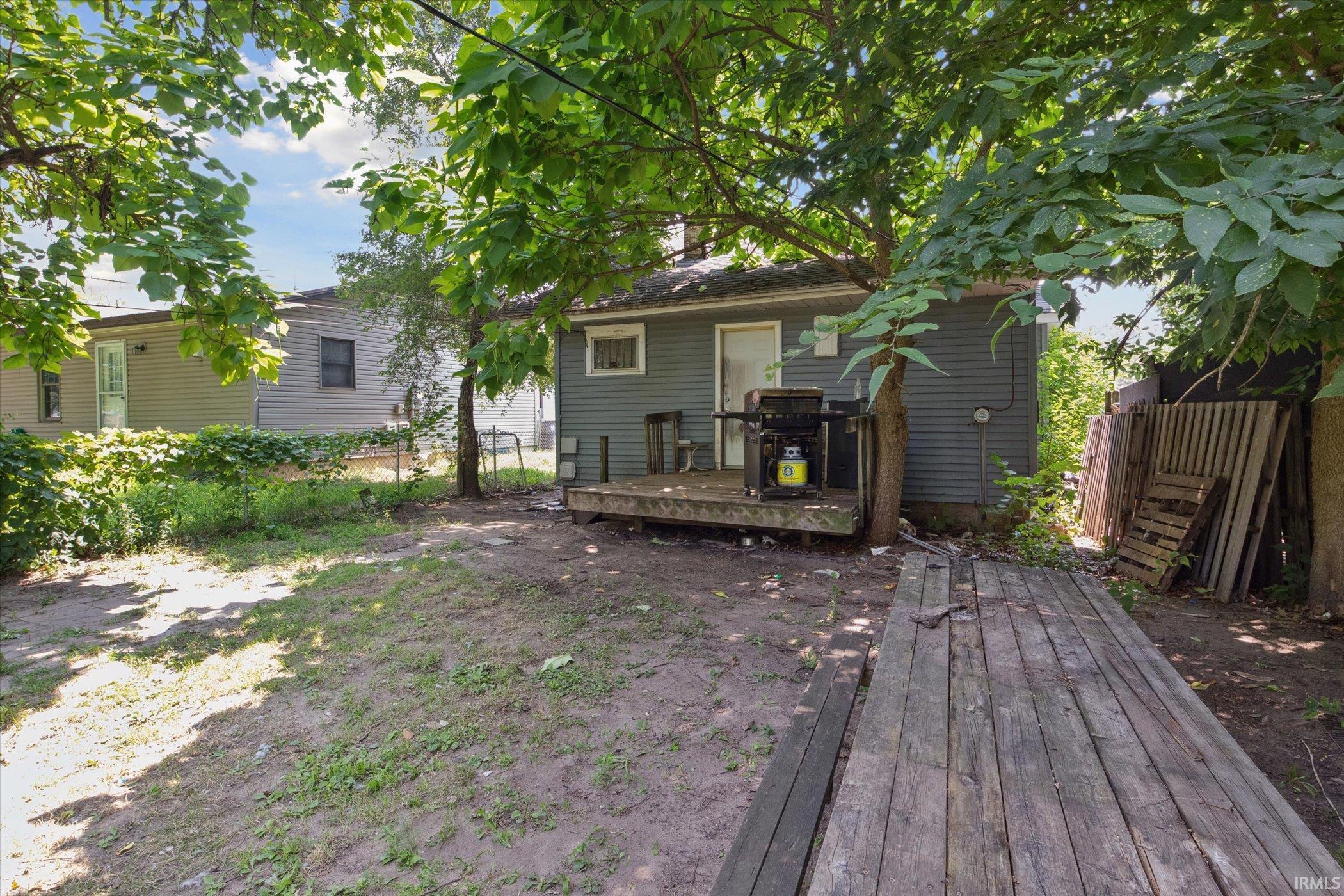 Rear exterior featuring a grey siding, a wooden deck, and mature trees