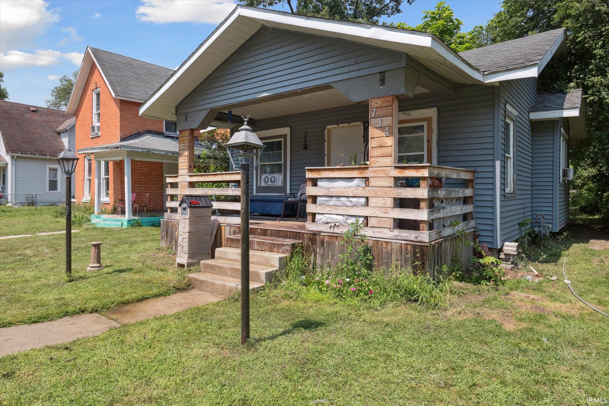 Front exterior featuring horizontal siding, a covered porch with a wood railing, concrete steps, a concrete walkway, and a landscaped yard
